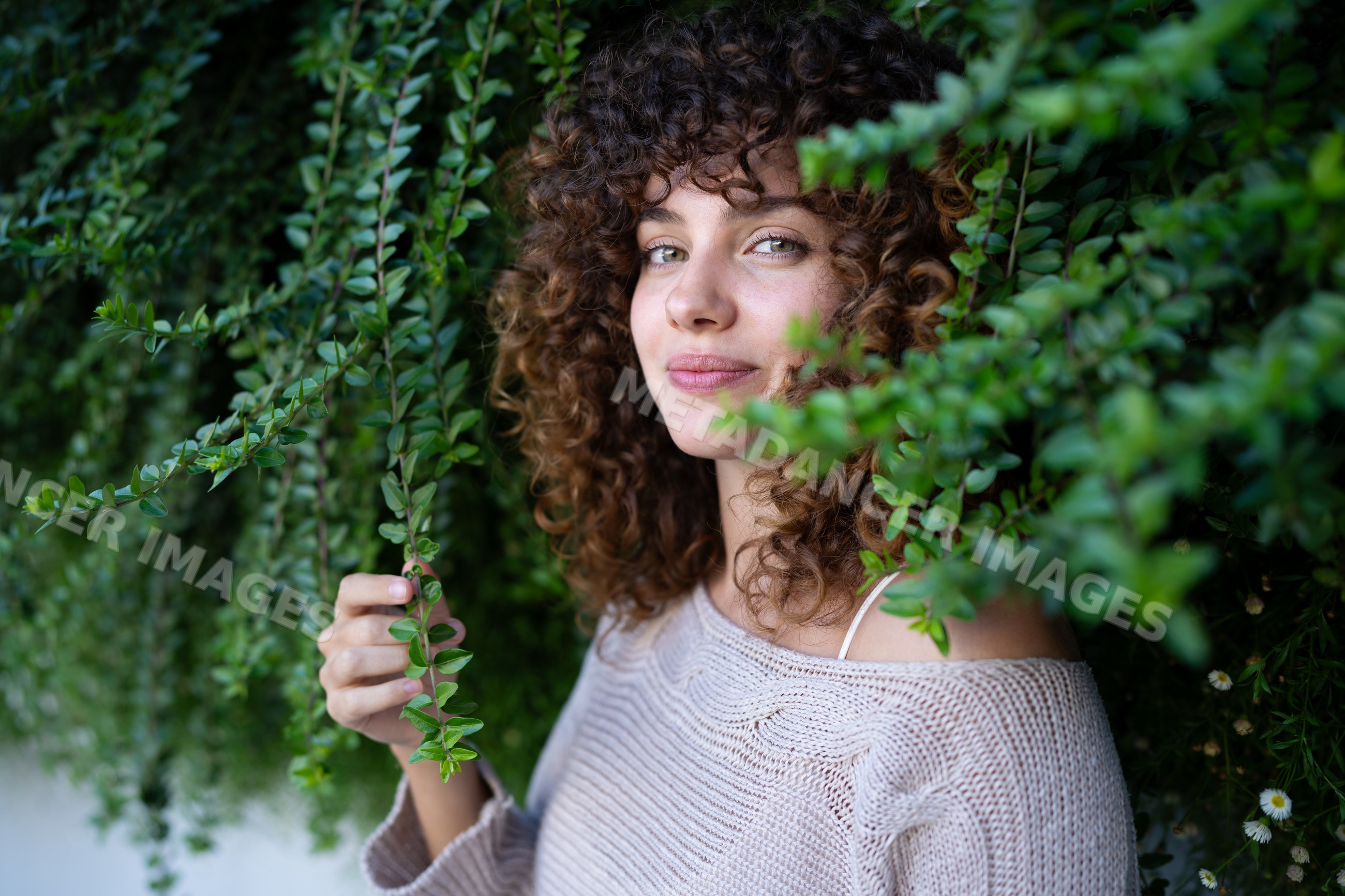 White woman with curly hair smiling outdoors holding green leaves