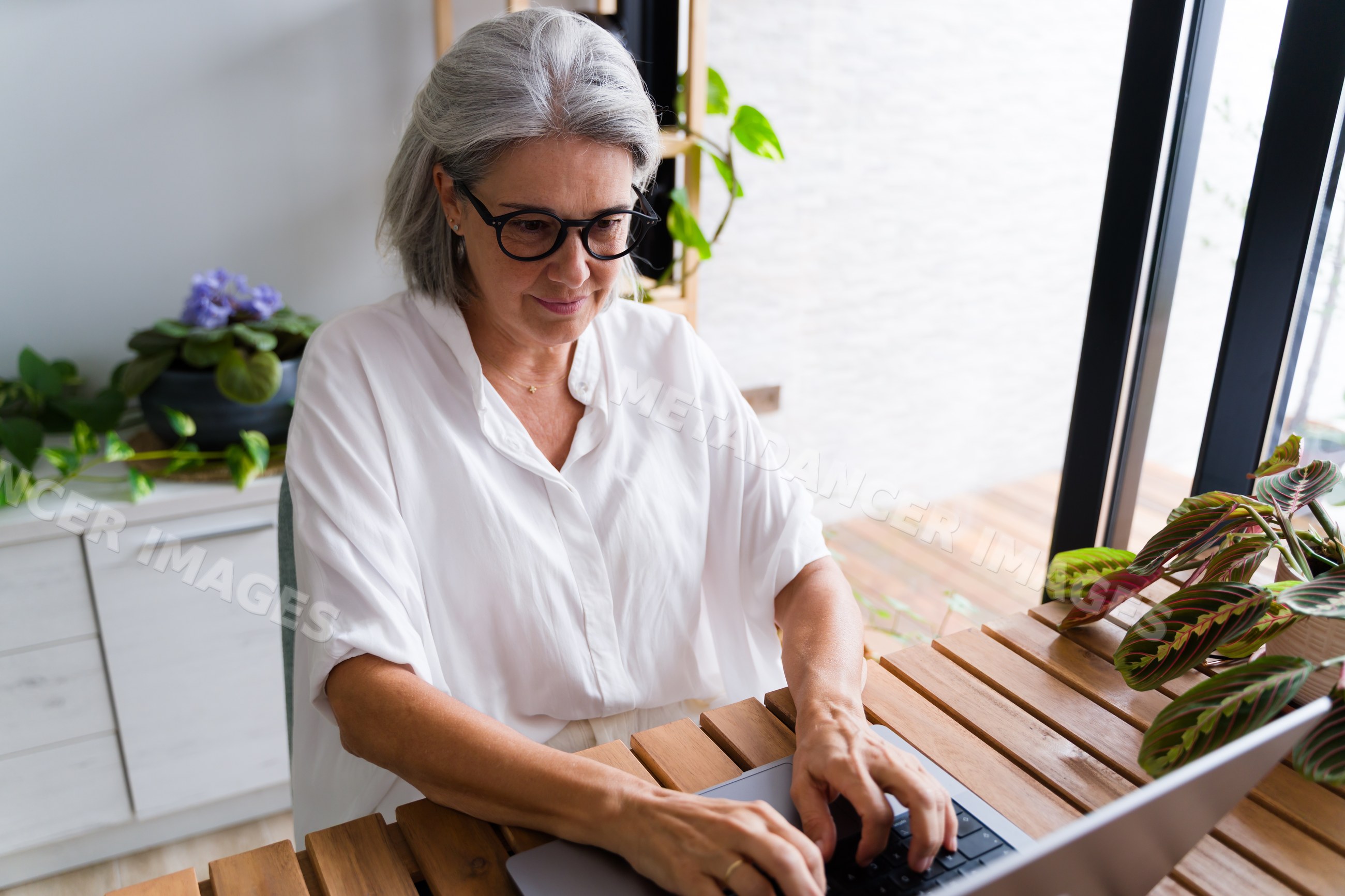 White Woman typing on laptop at wooden desk in home office with plants