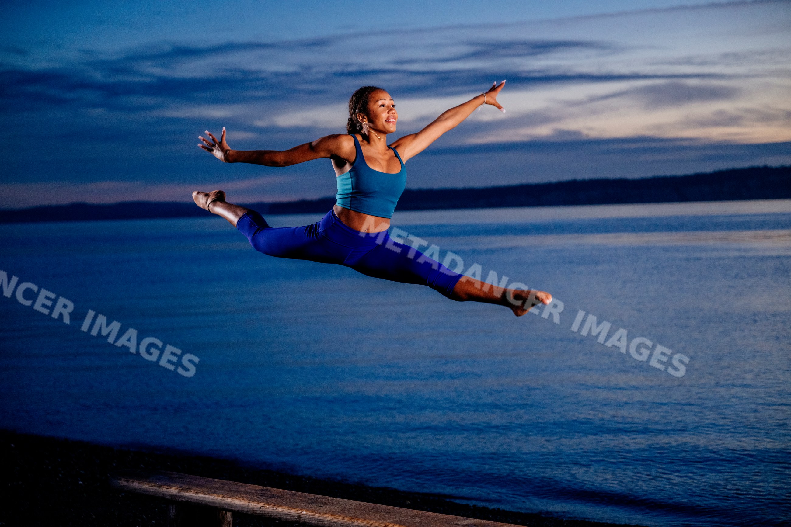 Hispanic woman performing yoga acrobatic leap by the ocean at sunset