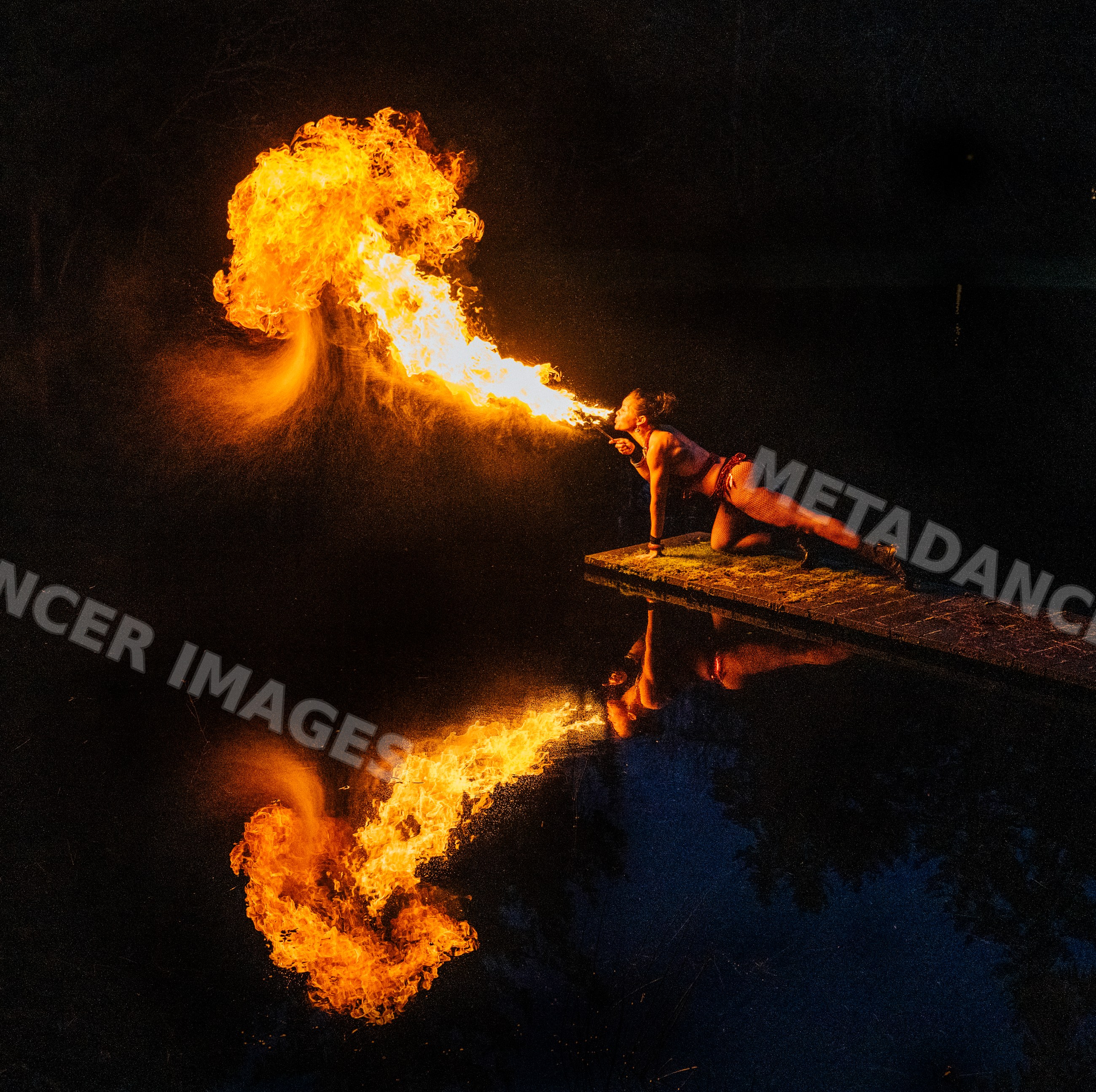 Fire breather performing on dock at night with flame reflection