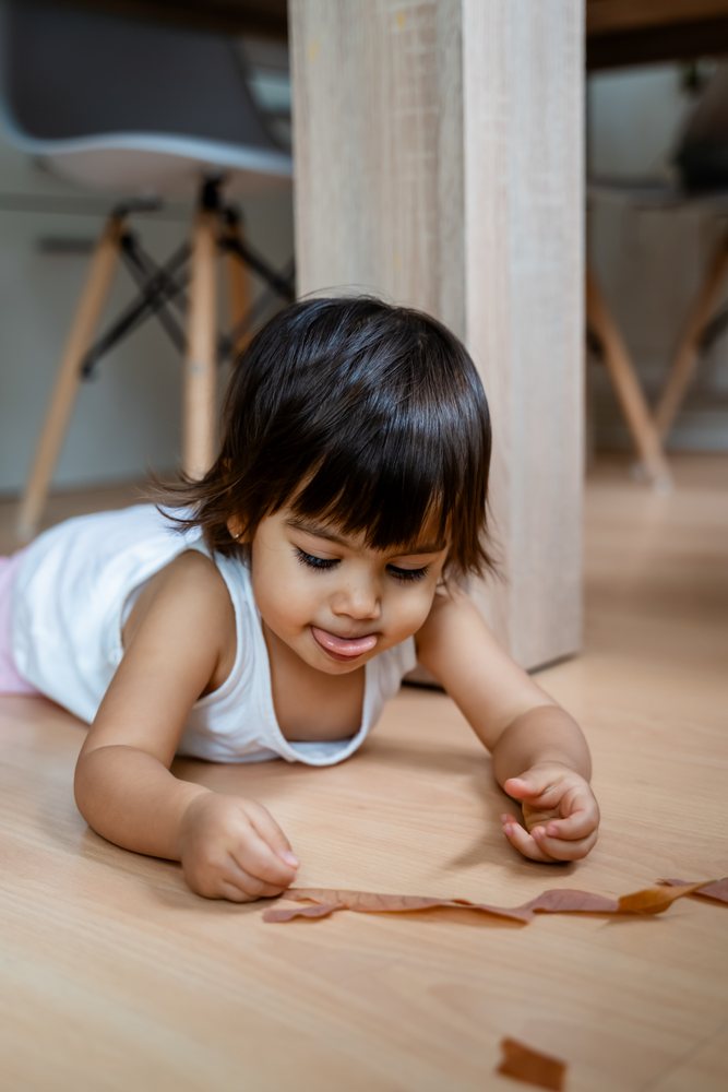 Toddler playing on wooden floor indoors near table legs in Spain