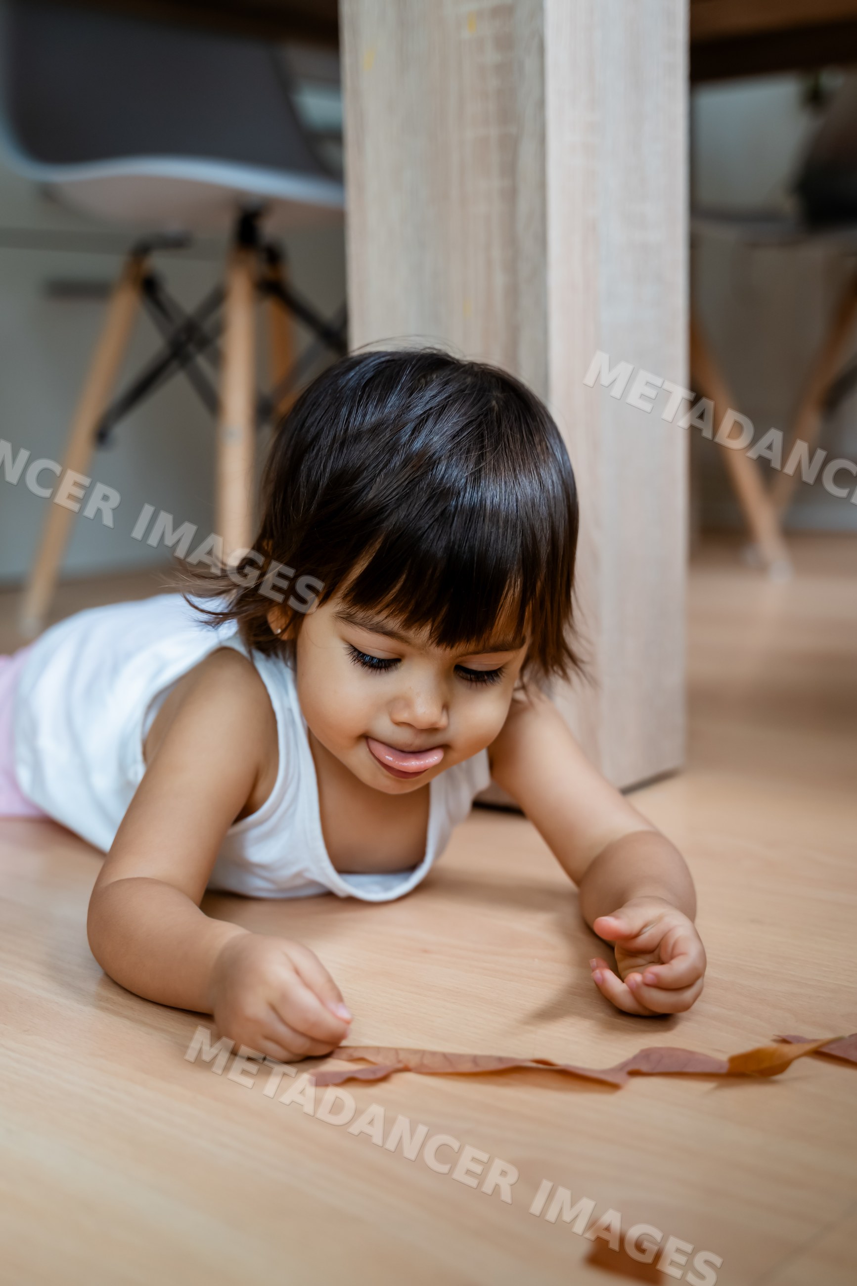 Toddler playing on wooden floor indoors near table legs in Spain