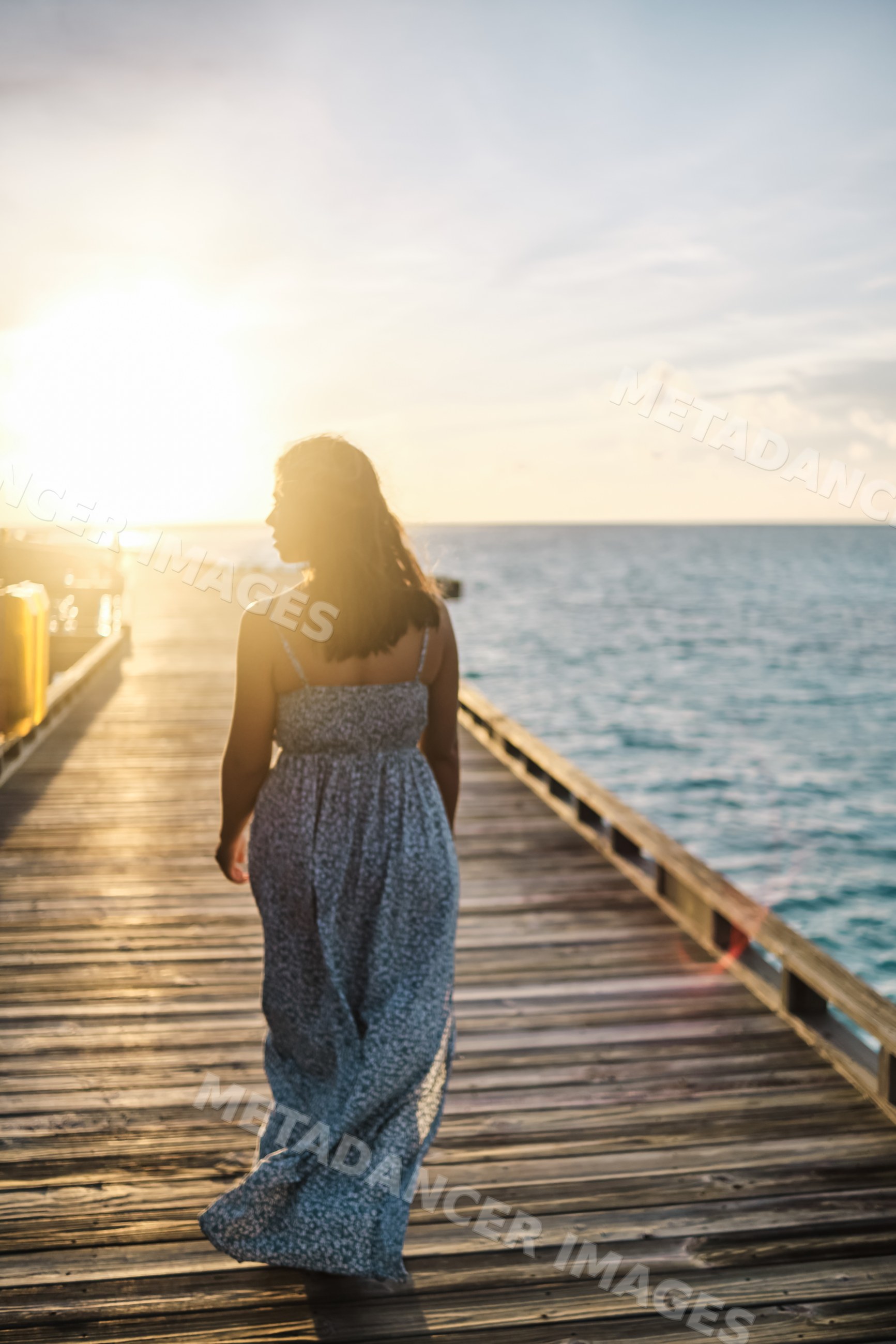 A white woman walking on a wooden pier at sunset by the sea