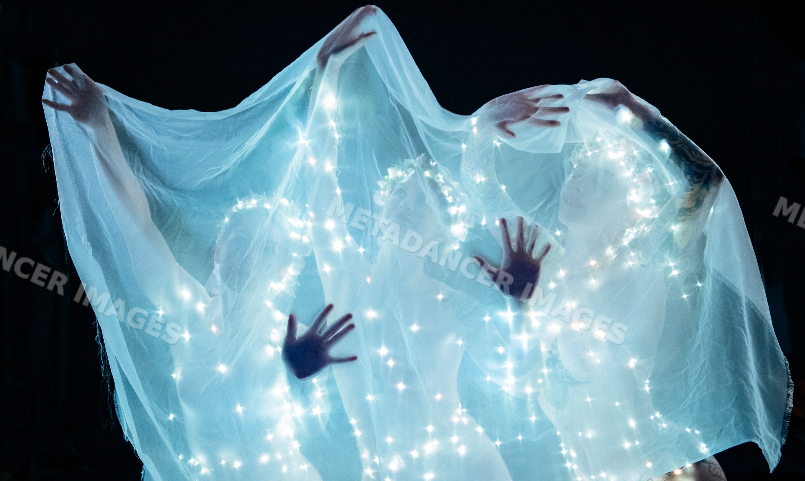 Three muses illuminated with glowing veils in artistic performance