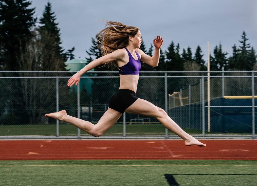 White female athlete jumping in mid-air on outdoor running track