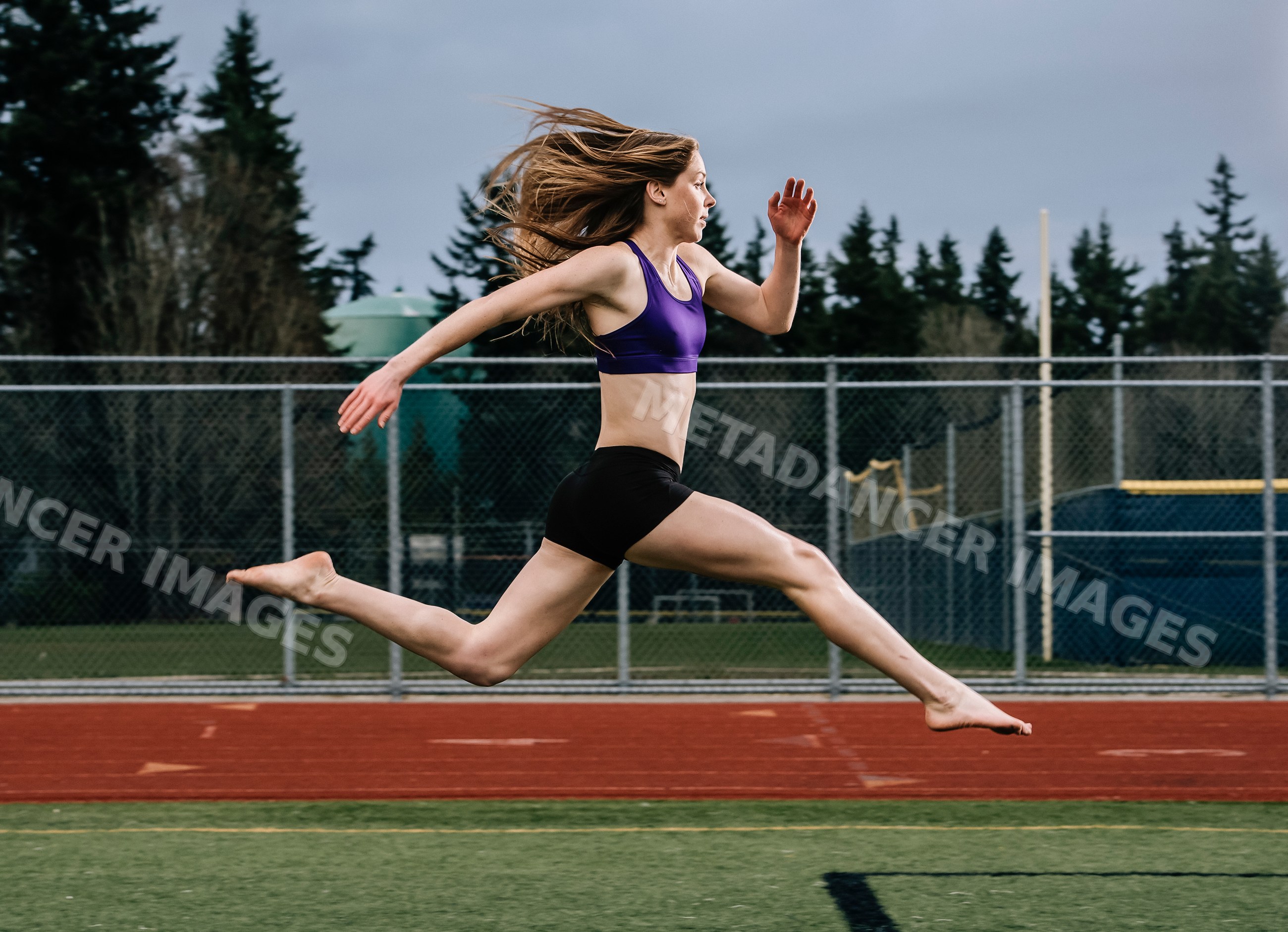 White female athlete jumping in mid-air on outdoor running track