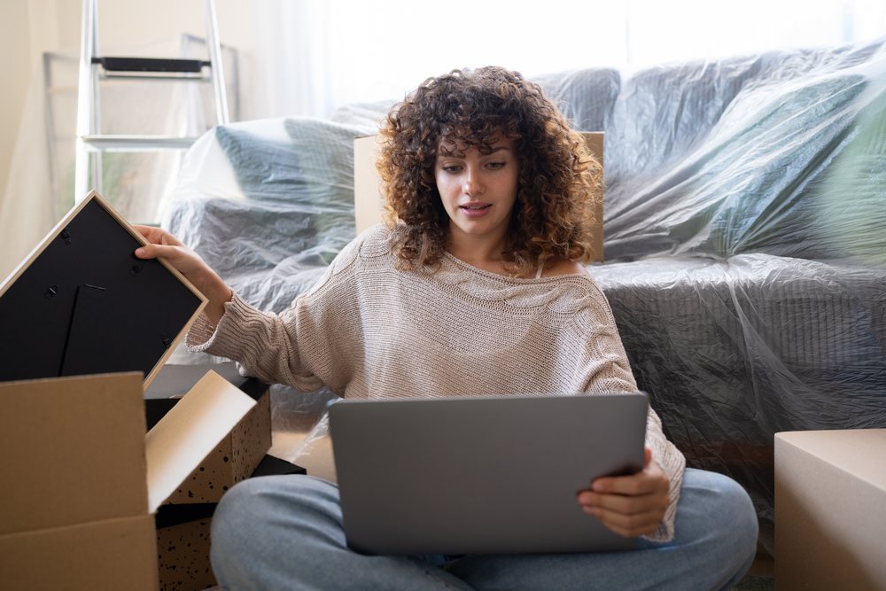 White woman using laptop while moving with packed boxes and covered