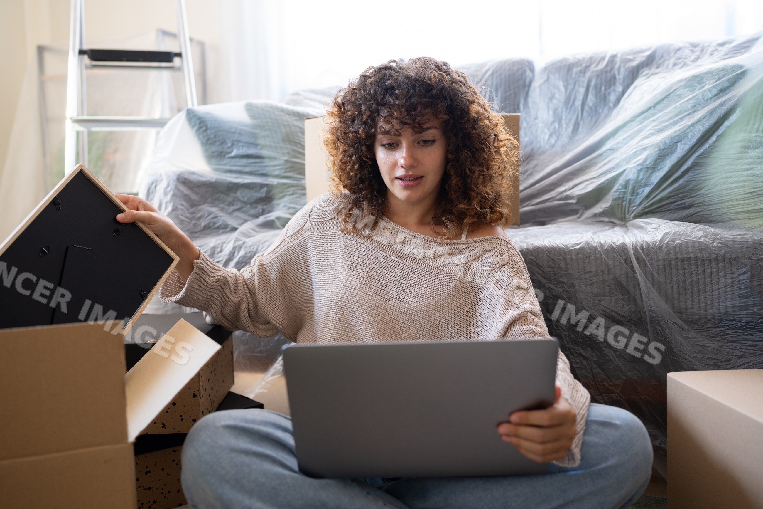 White woman using laptop while moving with packed boxes and covered