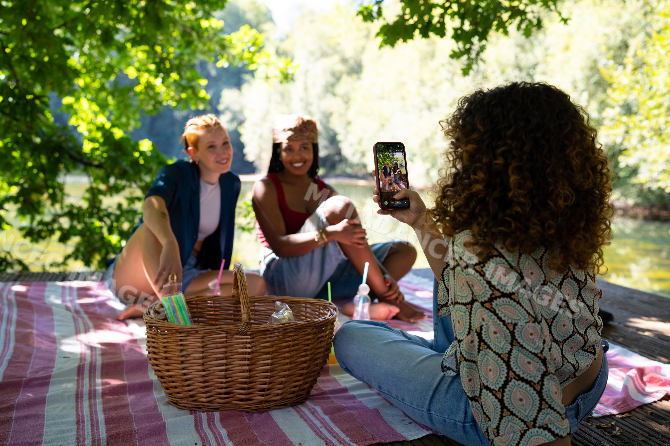 Friends enjoying picnic by river with smartphone outdoors