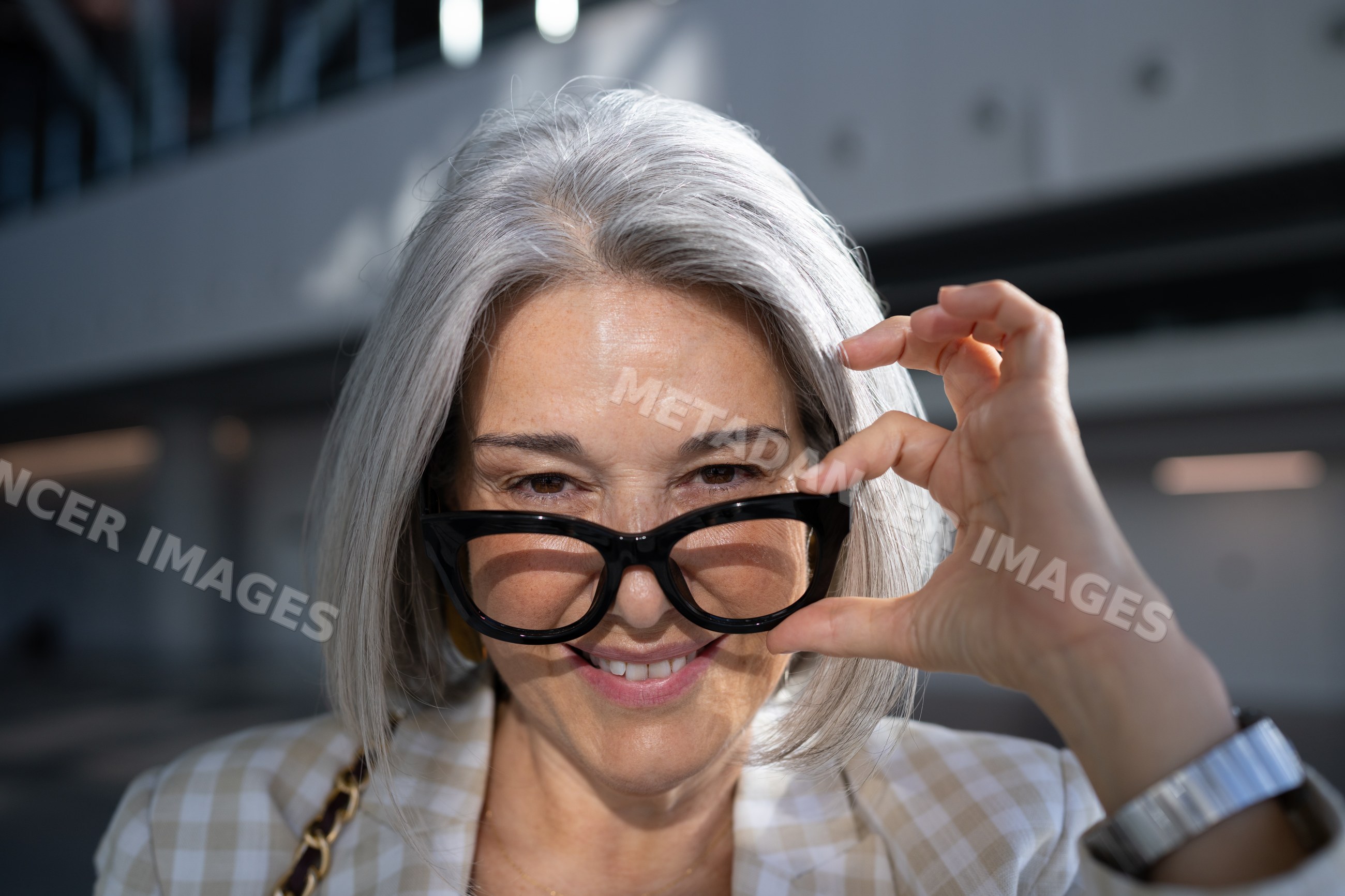 White woman with gray hair adjusting eyeglasses outdoors