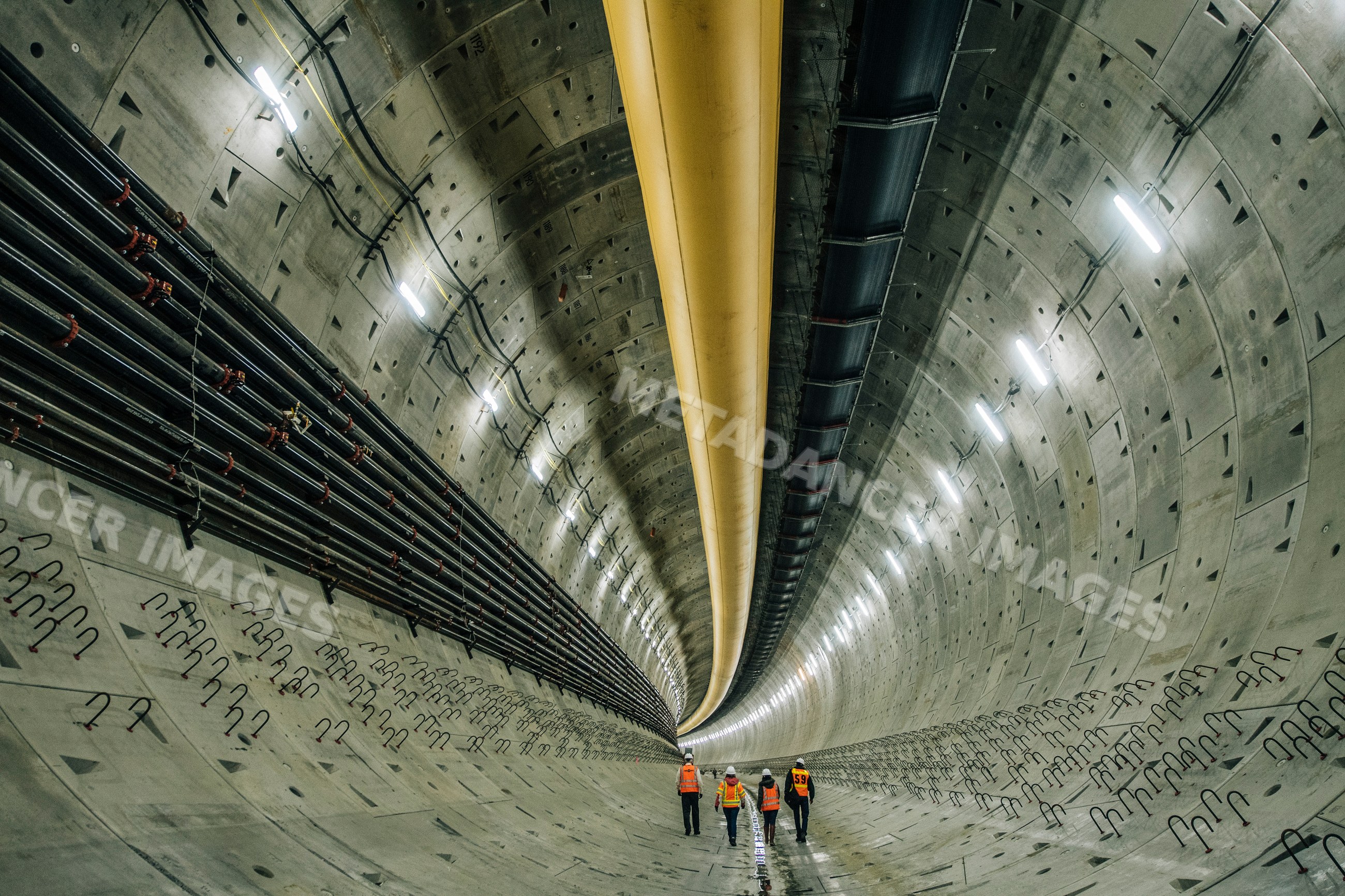 Four workers inspect a large concrete tunnel under construction