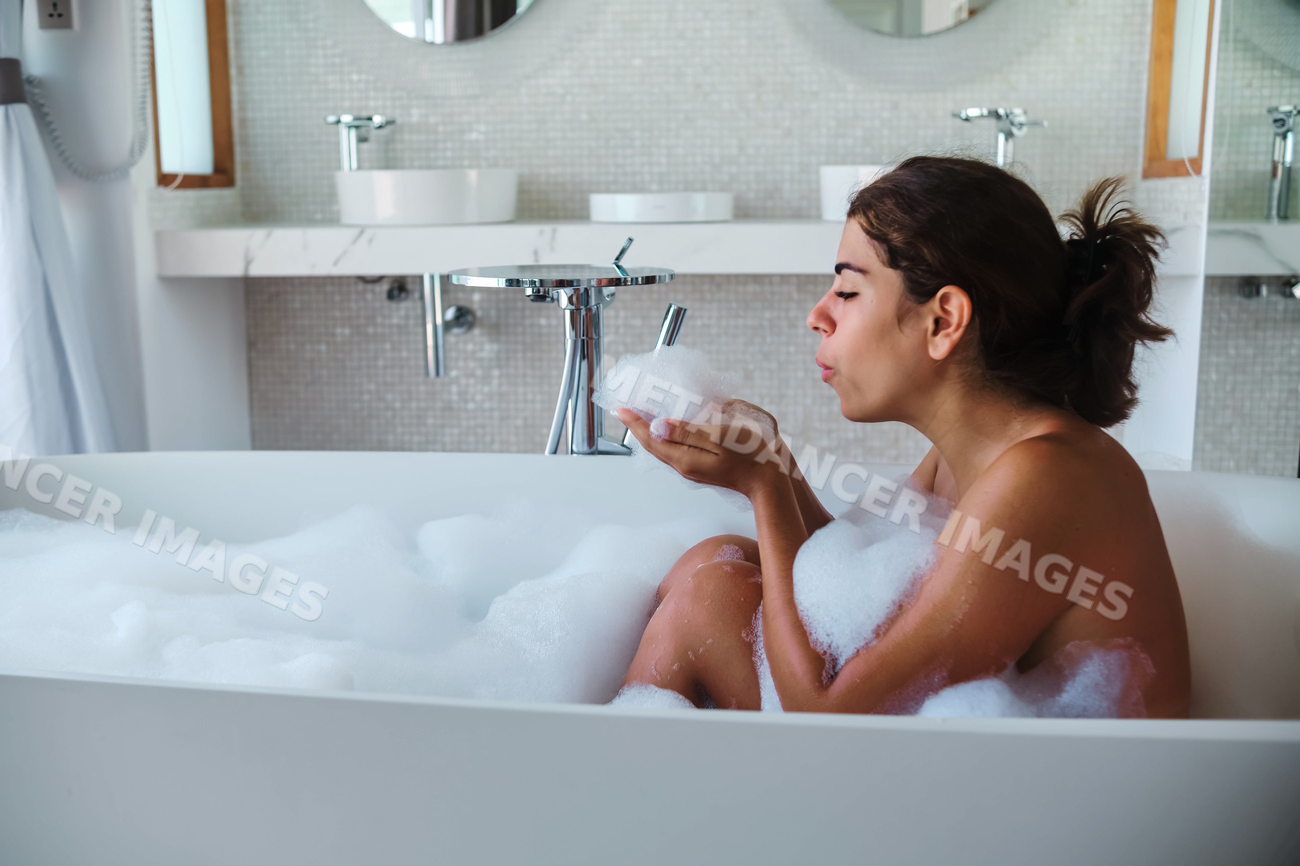 A white woman enjoys a relaxing bubble bath in a modern bathroom