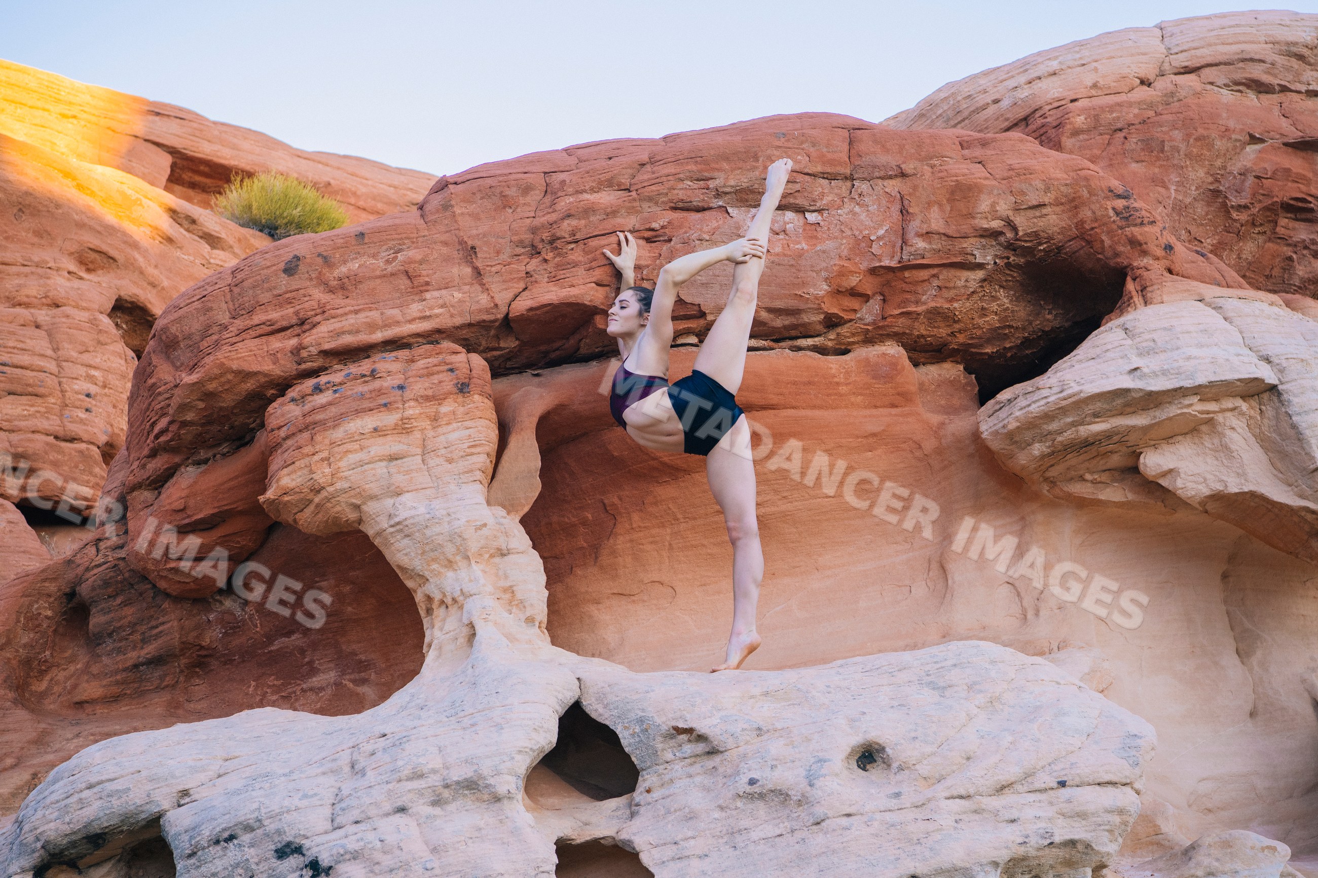 White woman performing yoga acrobatics on red rock formations