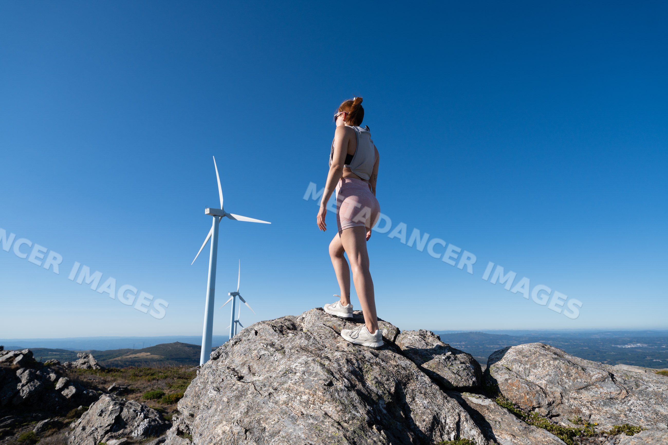White Woman standing on rock near wind turbines in Galicia Spain