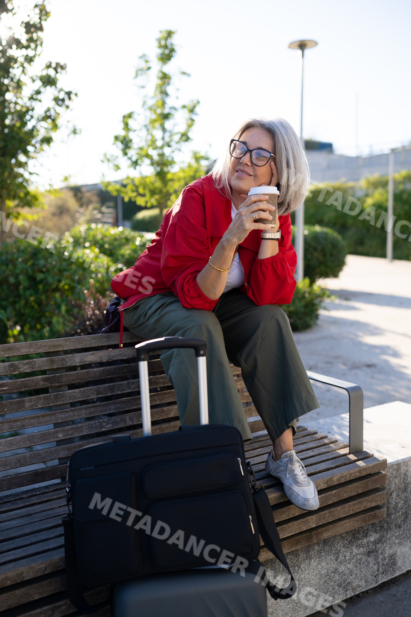 White woman sitting on bench with coffee and luggage outdoors