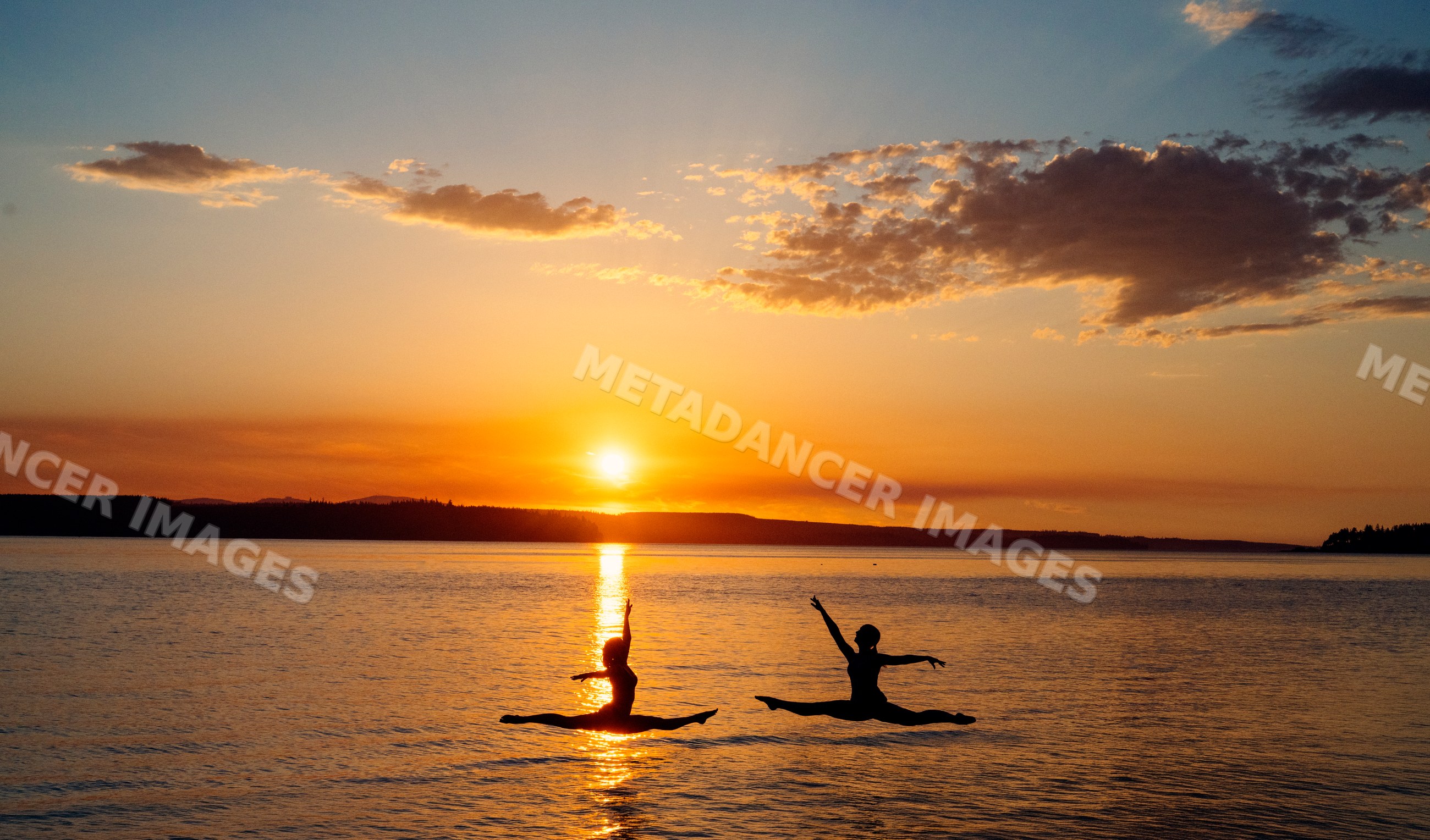 Two white people performing jumping split poses at sunset on a lake