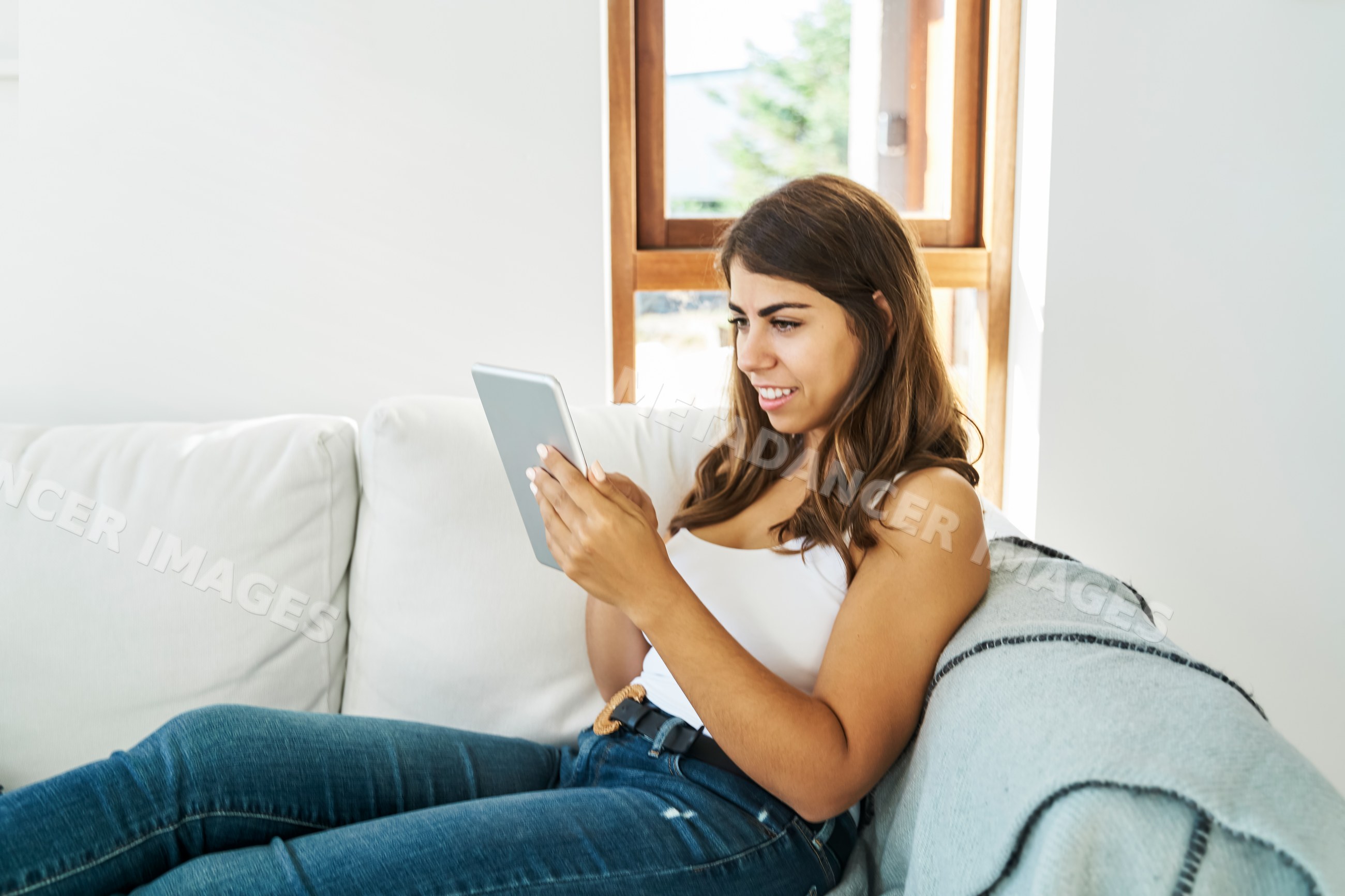 A white woman using a tablet while relaxing on a couch