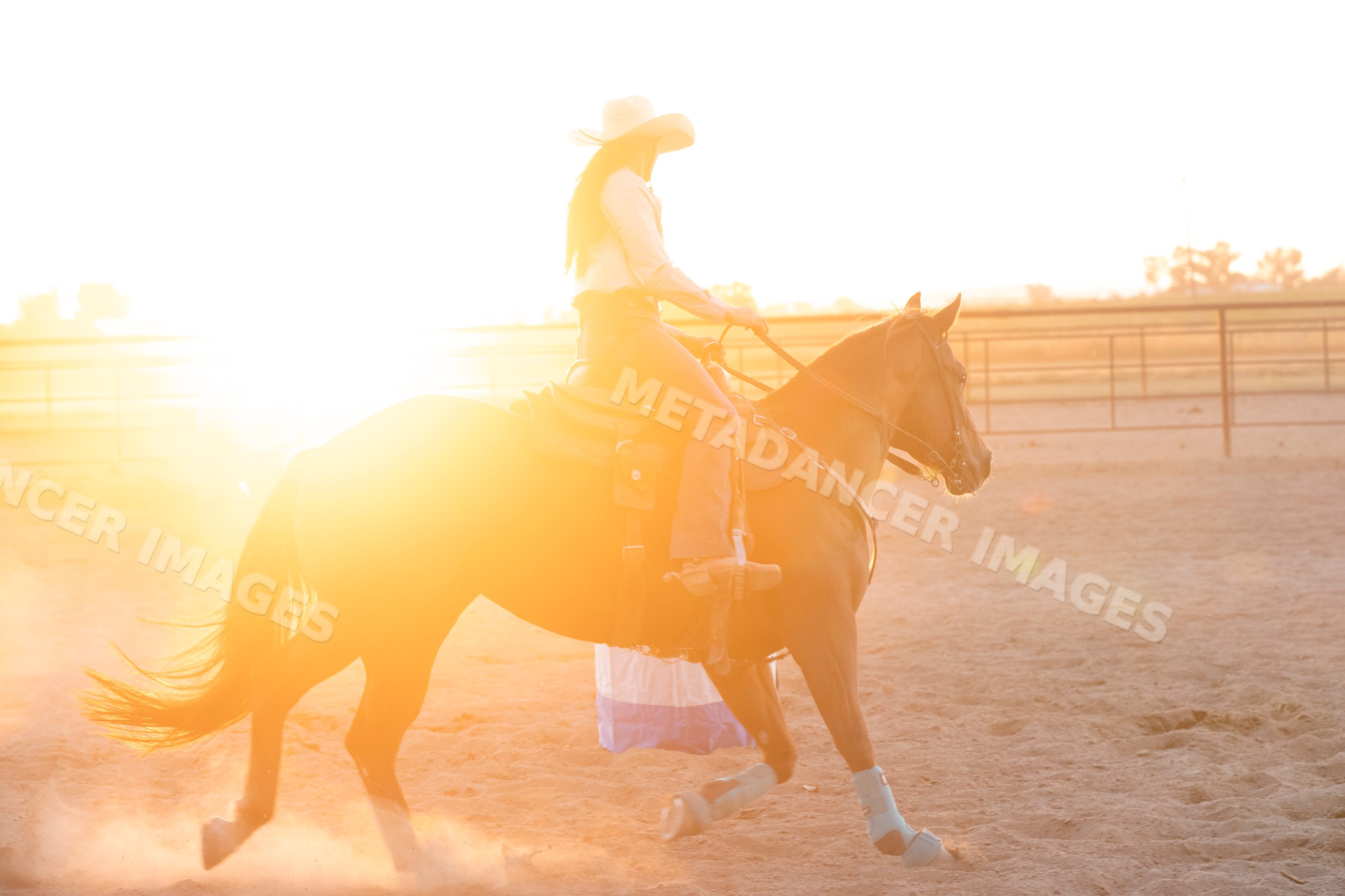 Horse rider wearing cowgirl hat riding in outdoor arena at sunset