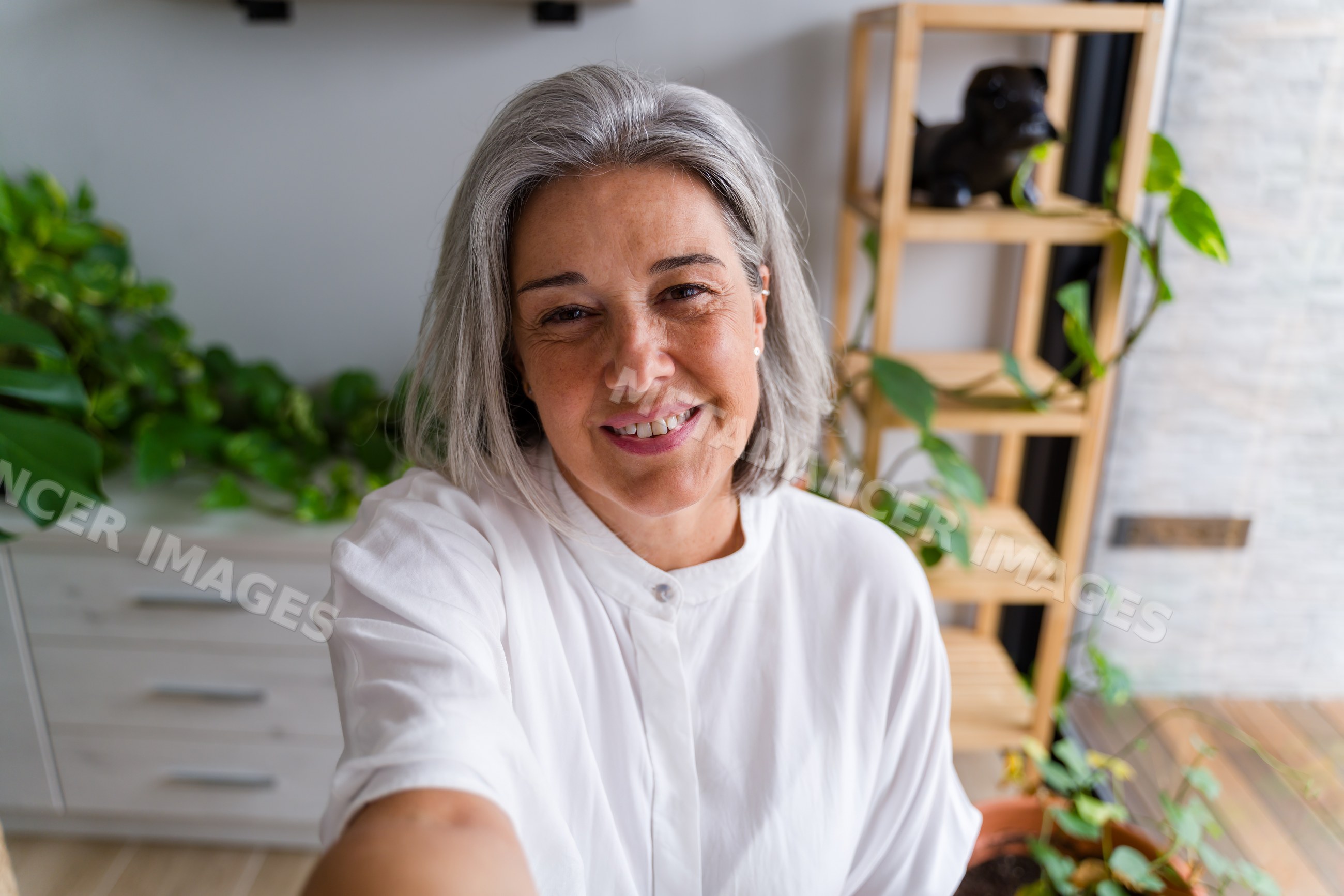 Middle aged white woman smiling and taking selfie indoors with plants