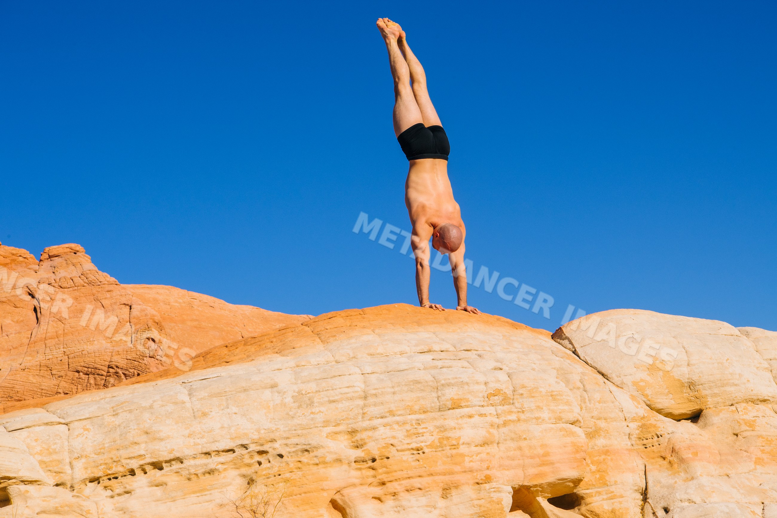 White man doing handstand exercise on rock formation outdoors
