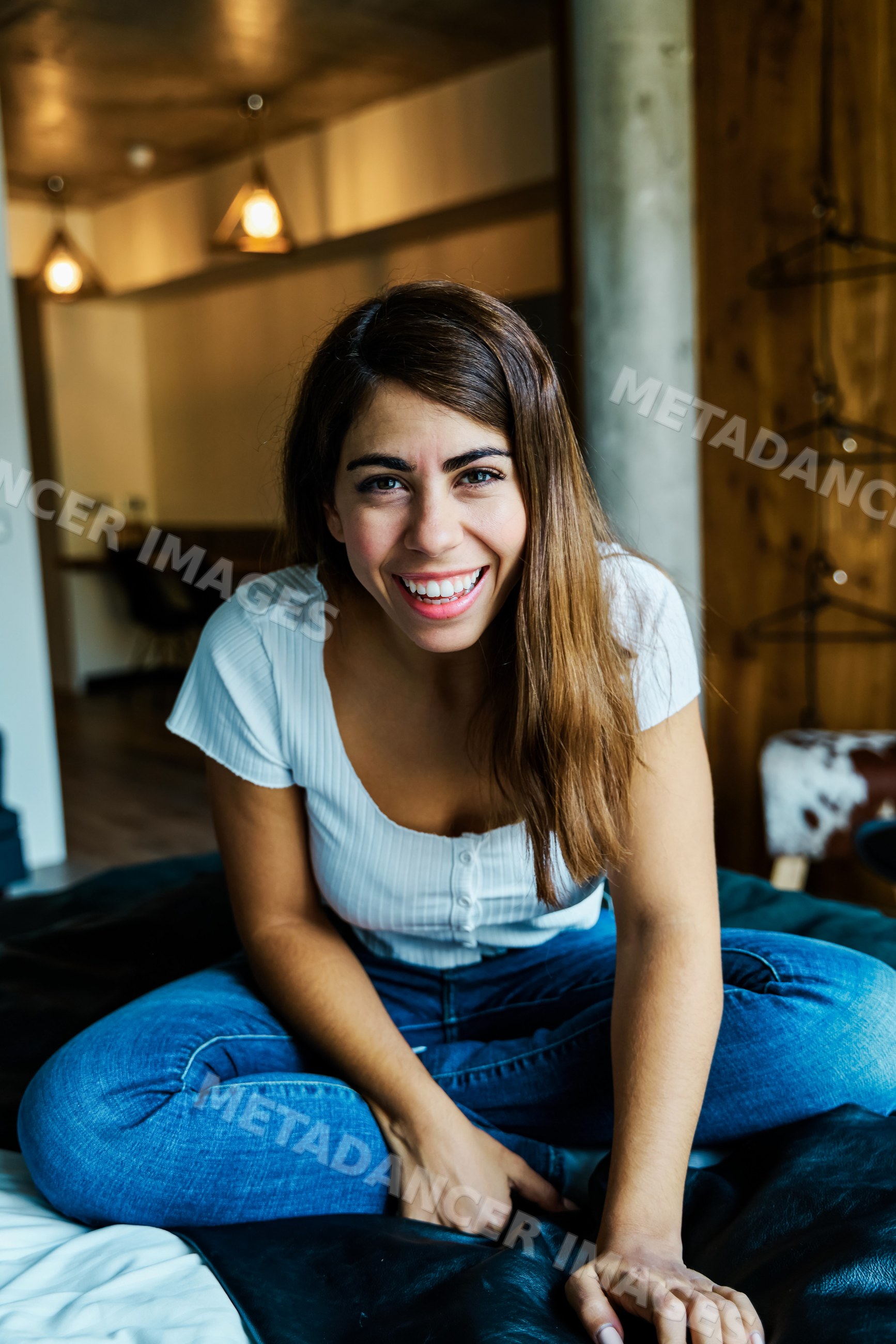 A young woman sitting on a bed smiling in a cozy hotel room in a hotel