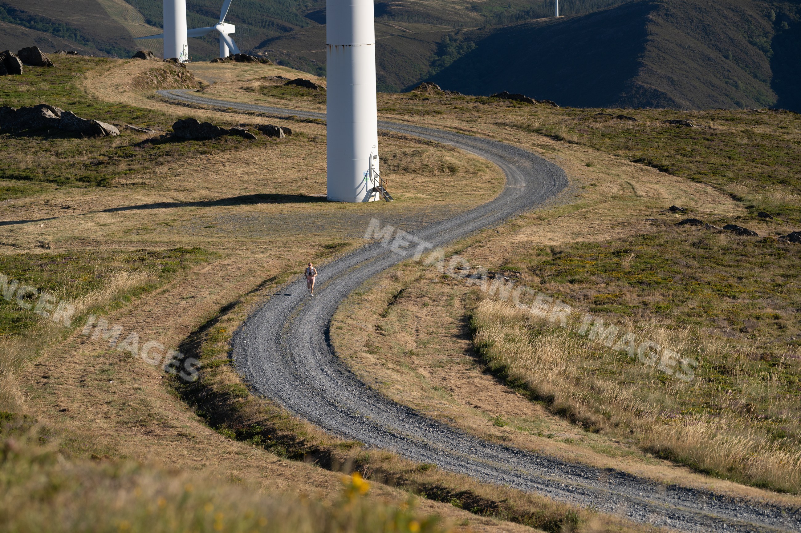 A white woman trail runs along a winding path beside wind turbines