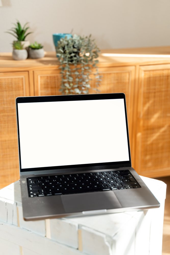 Laptop with blank screen on white crate indoors with wooden cabinet