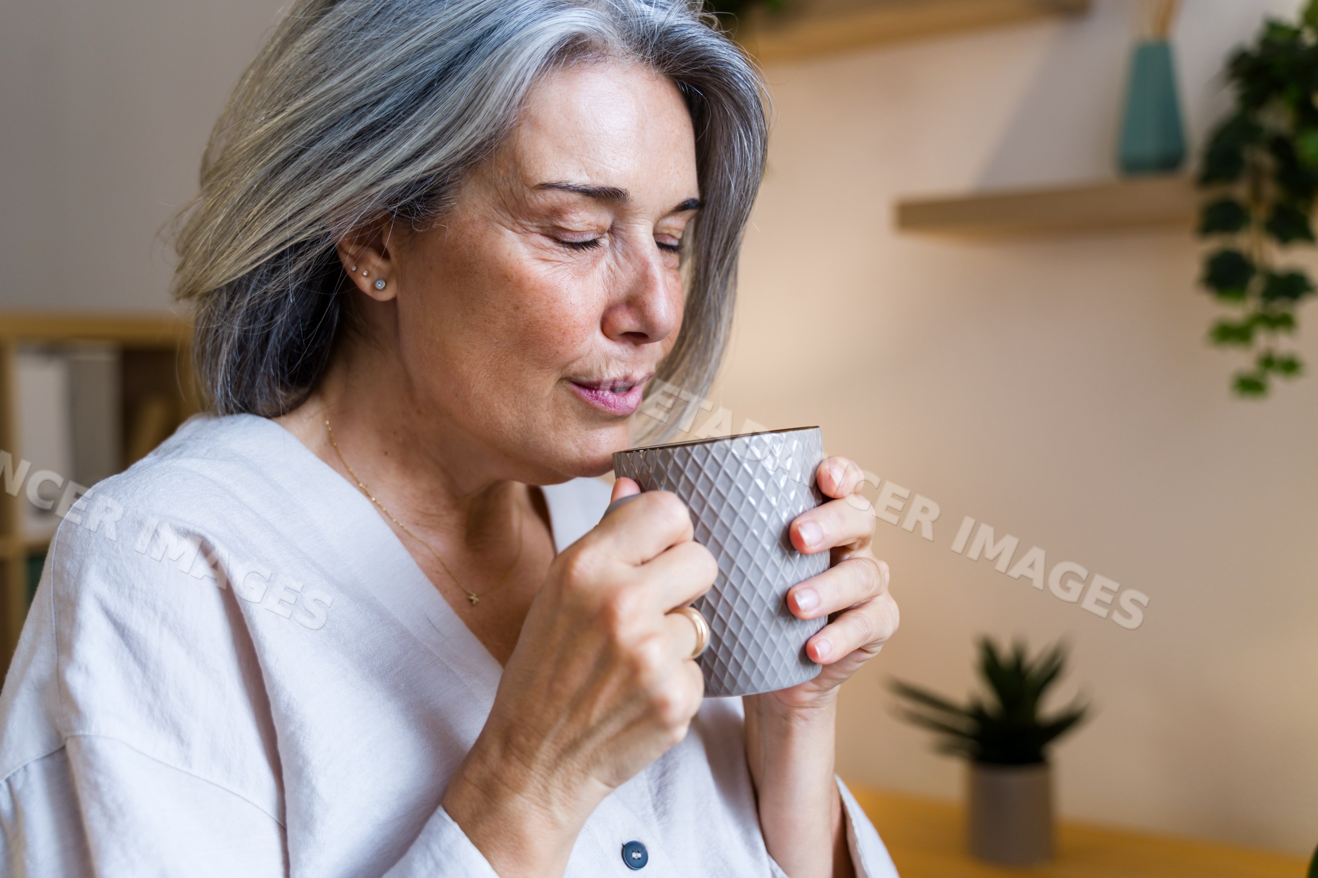 Mature white woman drinking warm beverage indoors with peaceful