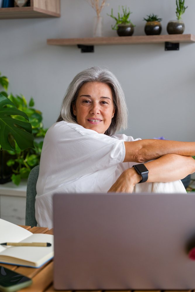 Middle-aged white woman using laptop in home office with plants