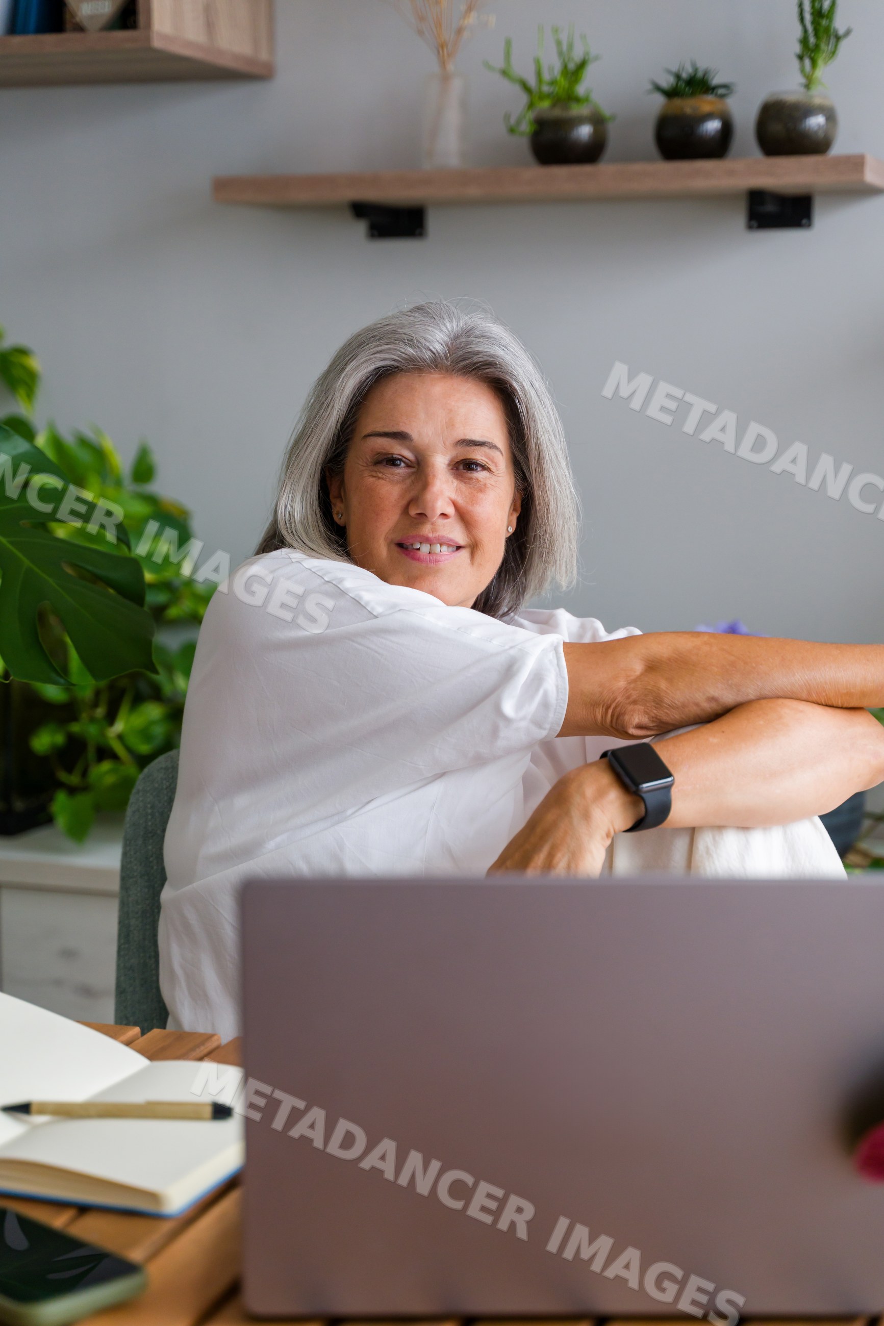 Middle-aged white woman using laptop in home office with plants