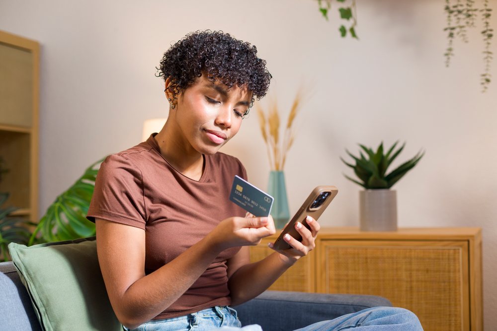 African American woman sitting on couch holding credit card using