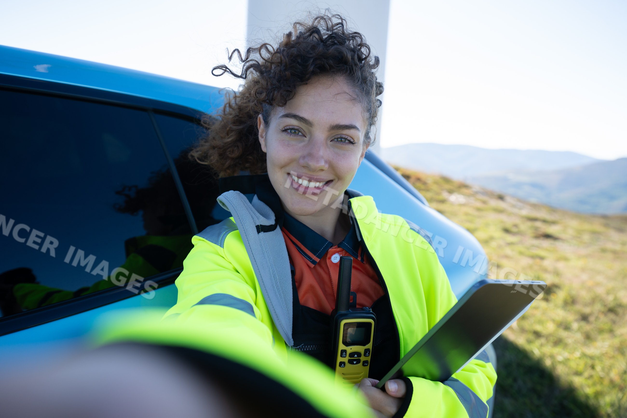 White woman taking selfie outdoors with tablet and walkie-talkie