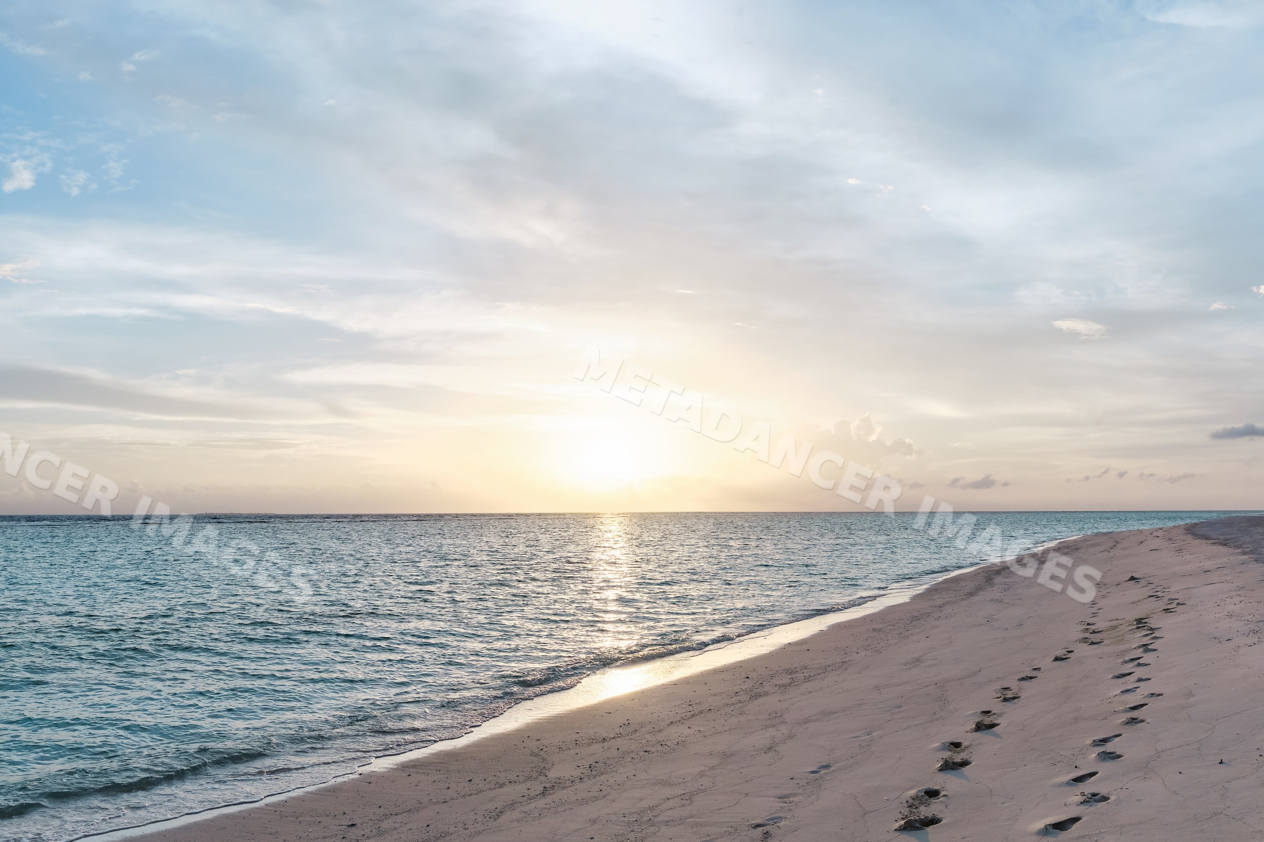 Sunset over a peaceful sandy beach with footprints in a beach