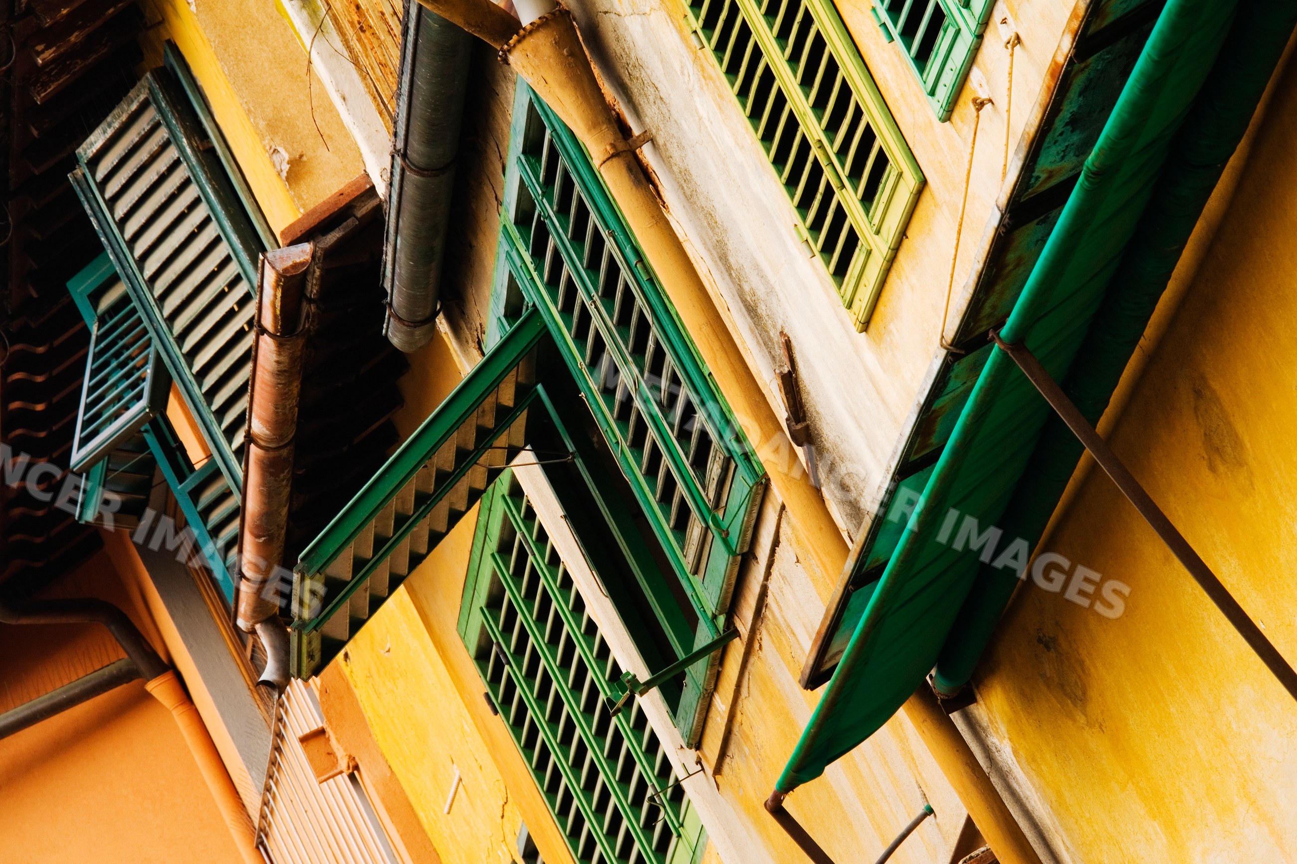 Green window shutters on historic yellow building, italy