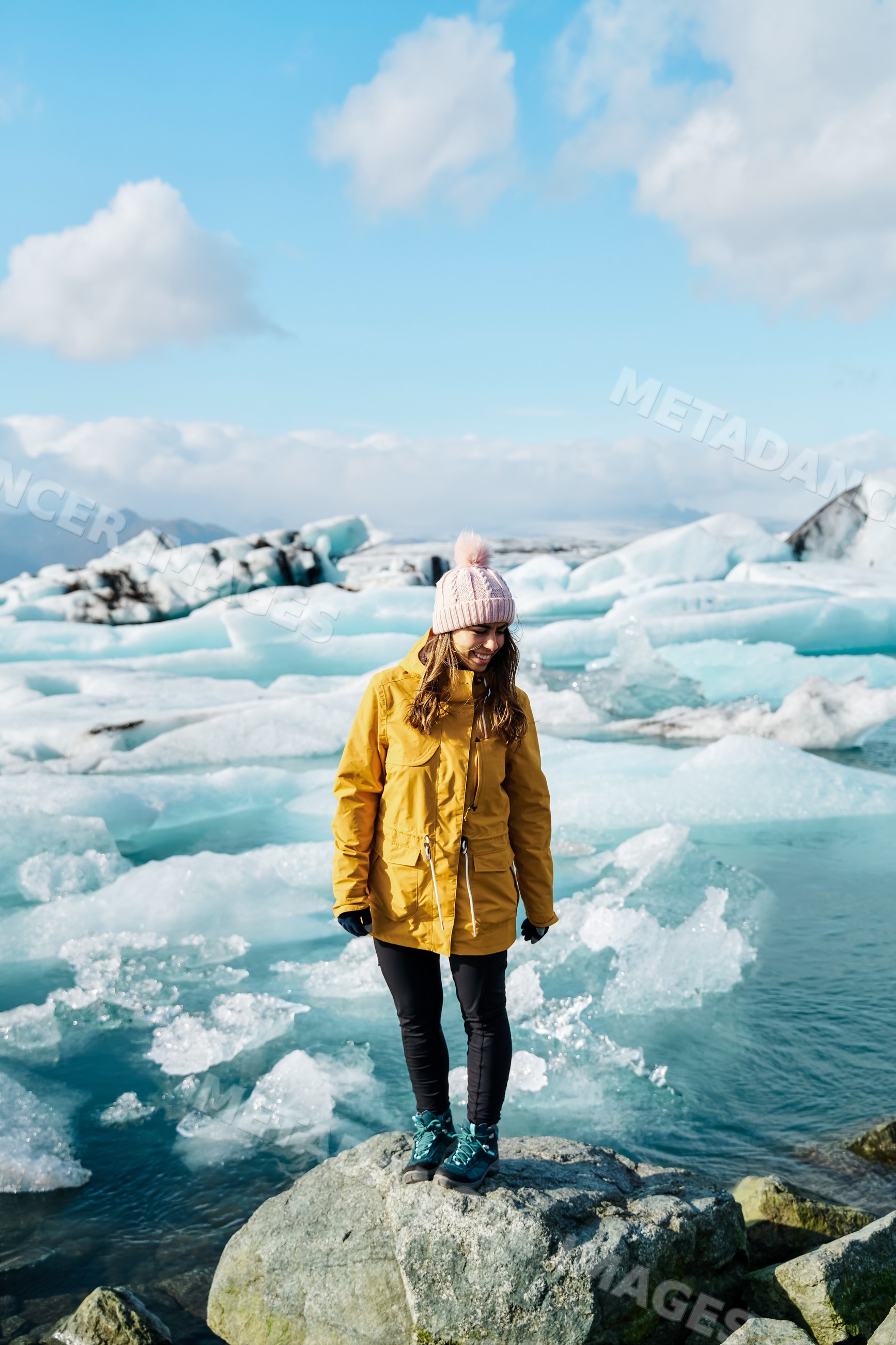 A white woman in winter clothing standing on a rock at a glacier