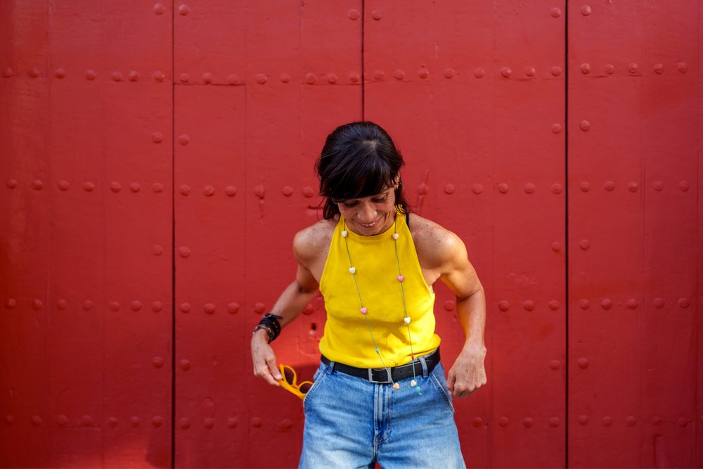 Hispanic woman in yellow tank top posing by red door in Málaga Spain
