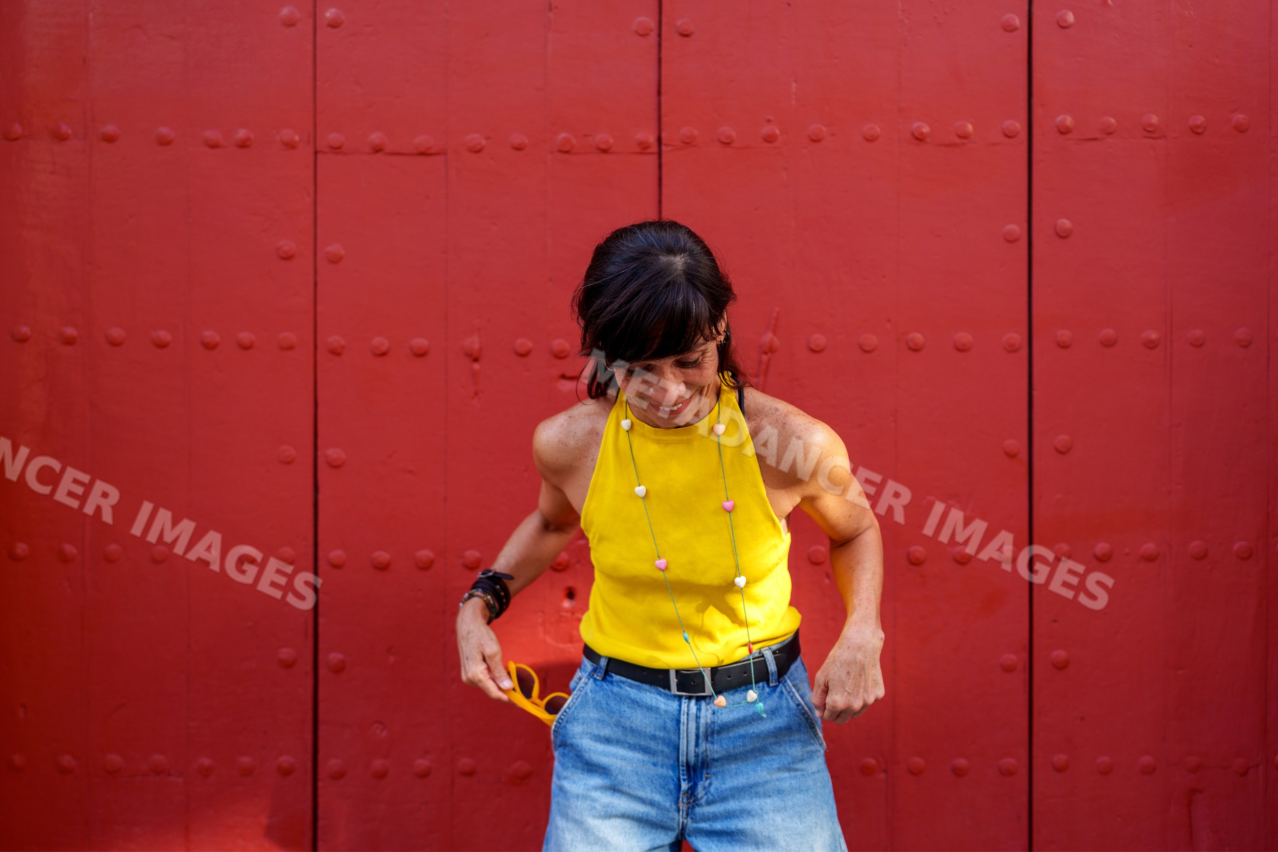 Hispanic woman in yellow tank top posing by red door in Málaga Spain
