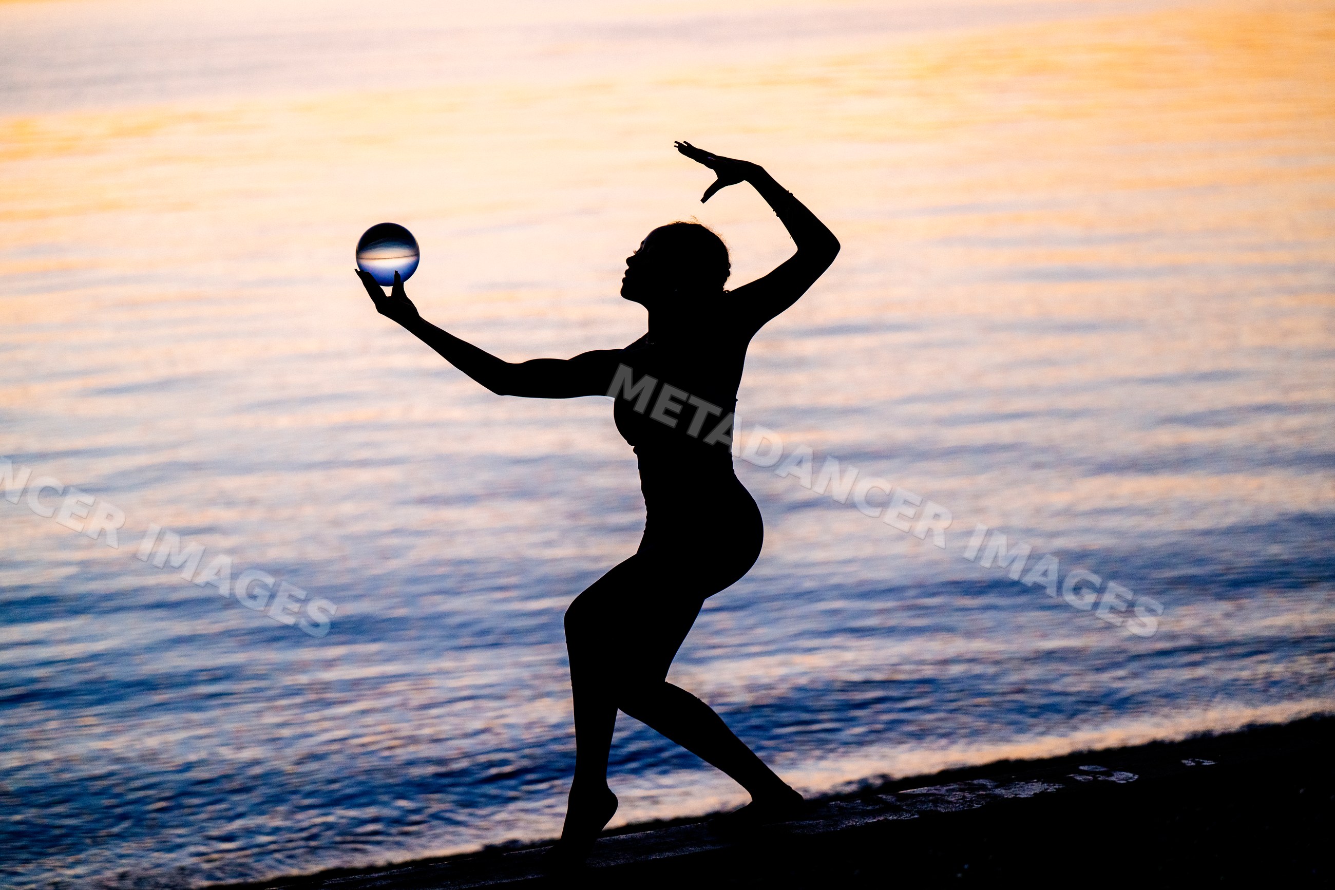 Hispanic woman practicing yoga acrobatics with ball on shore at sunset