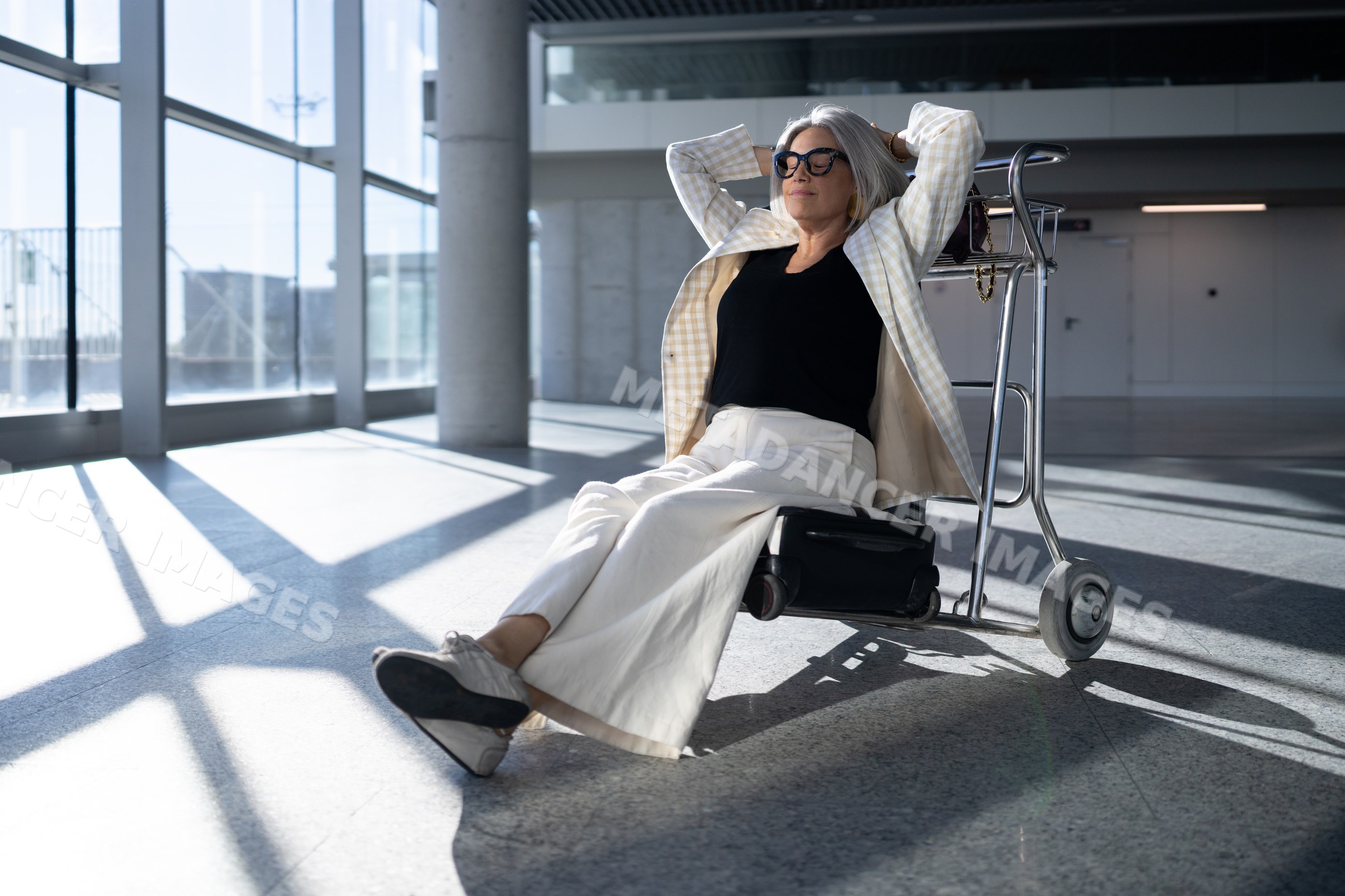 White woman relaxing seated on airport luggage cart in terminal