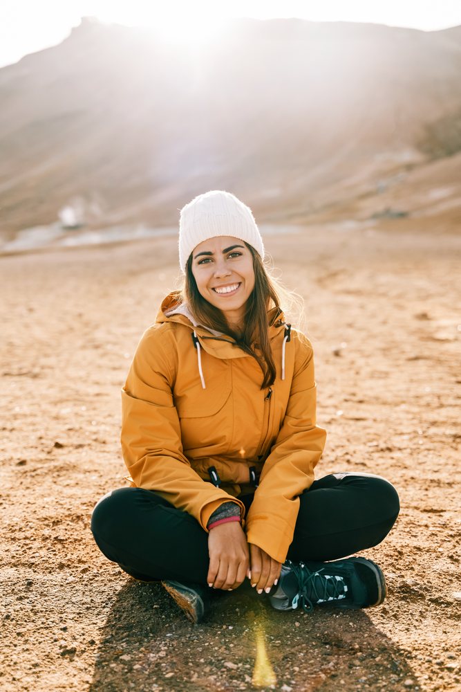 A white woman sits on rocky ground with sunlight