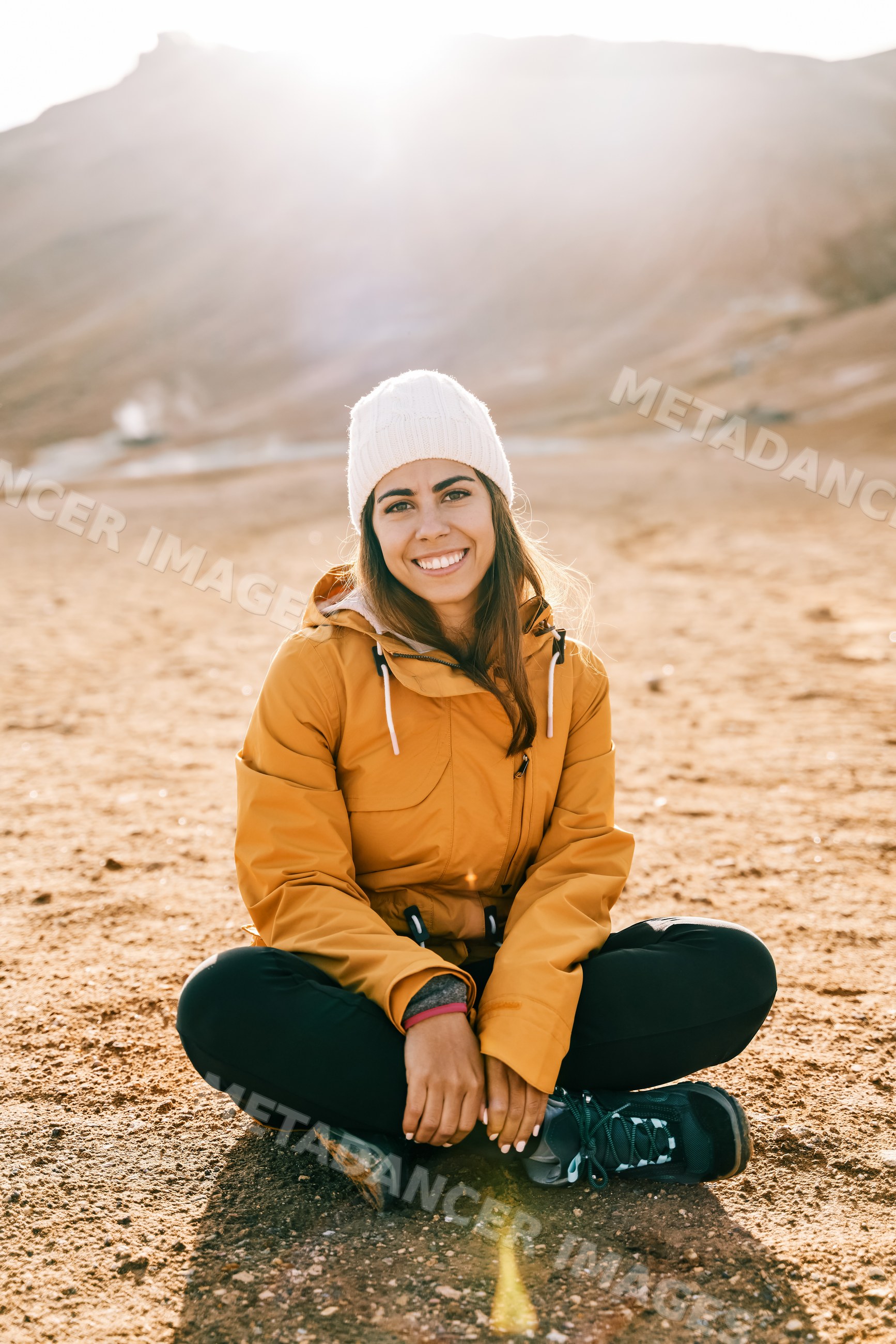 A white woman sits on rocky ground with sunlight