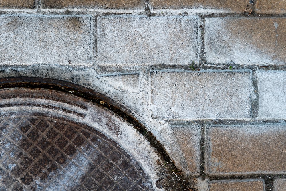 Metal manhole cover embedded in weathered concrete sidewalk pavement
