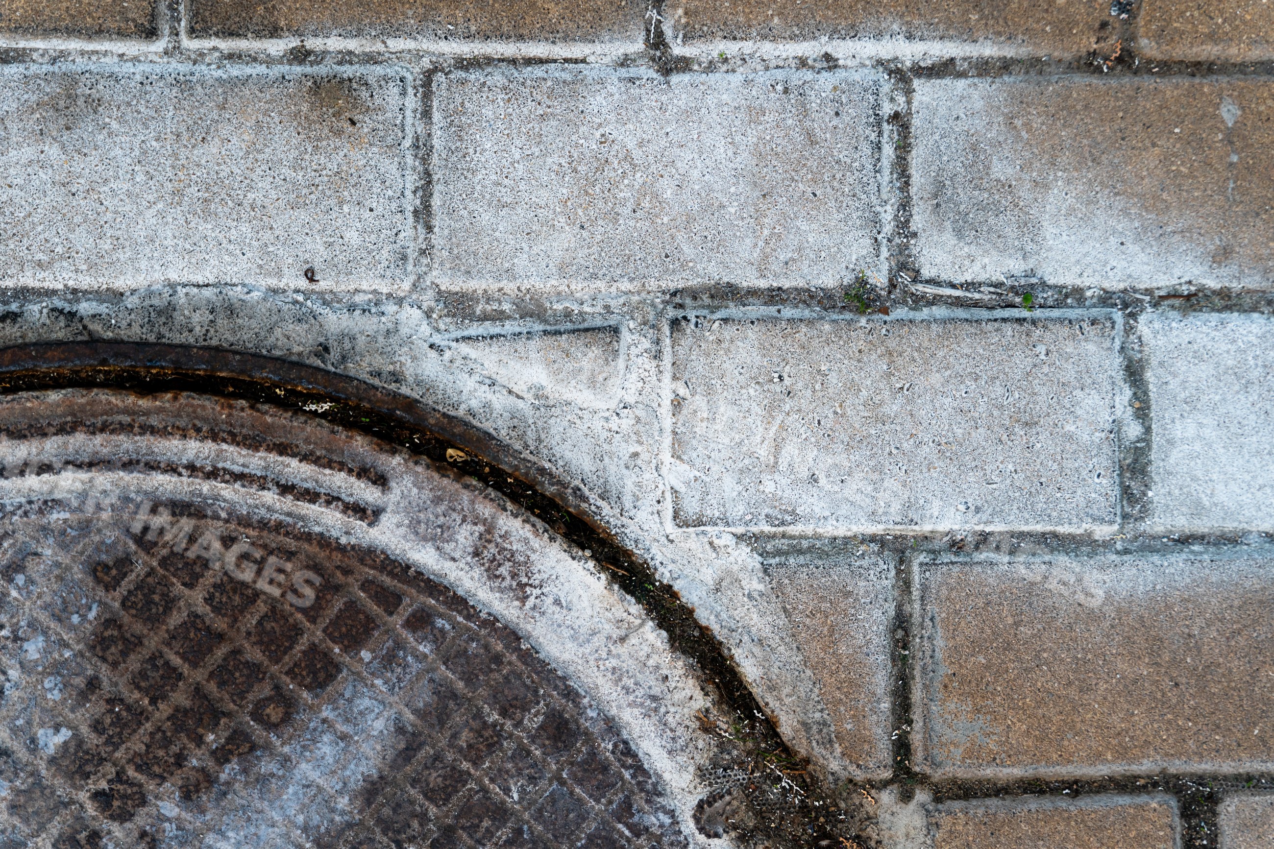 Metal manhole cover embedded in weathered concrete sidewalk pavement