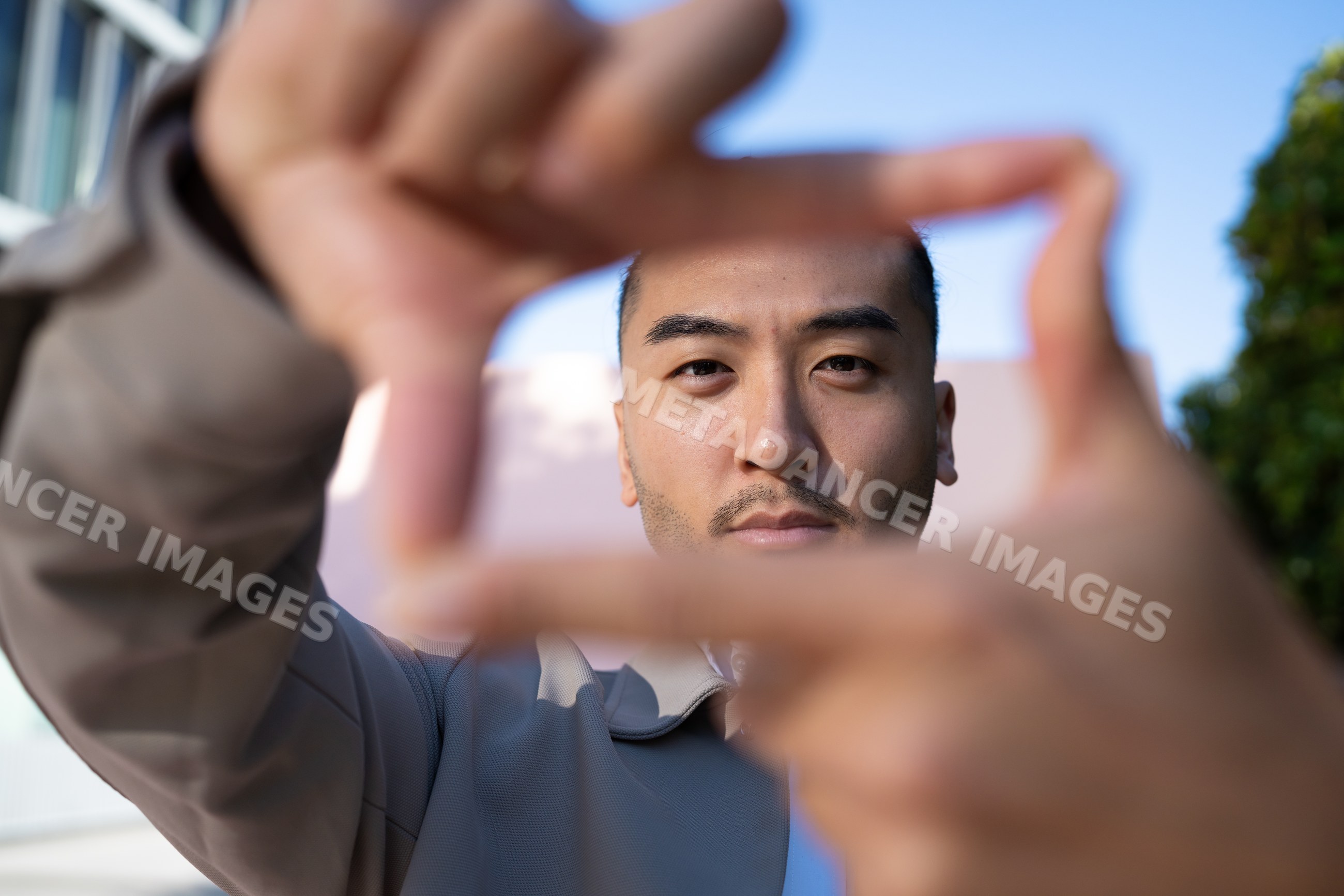 Man framing his face with hands outdoors under blue sky in Madrid