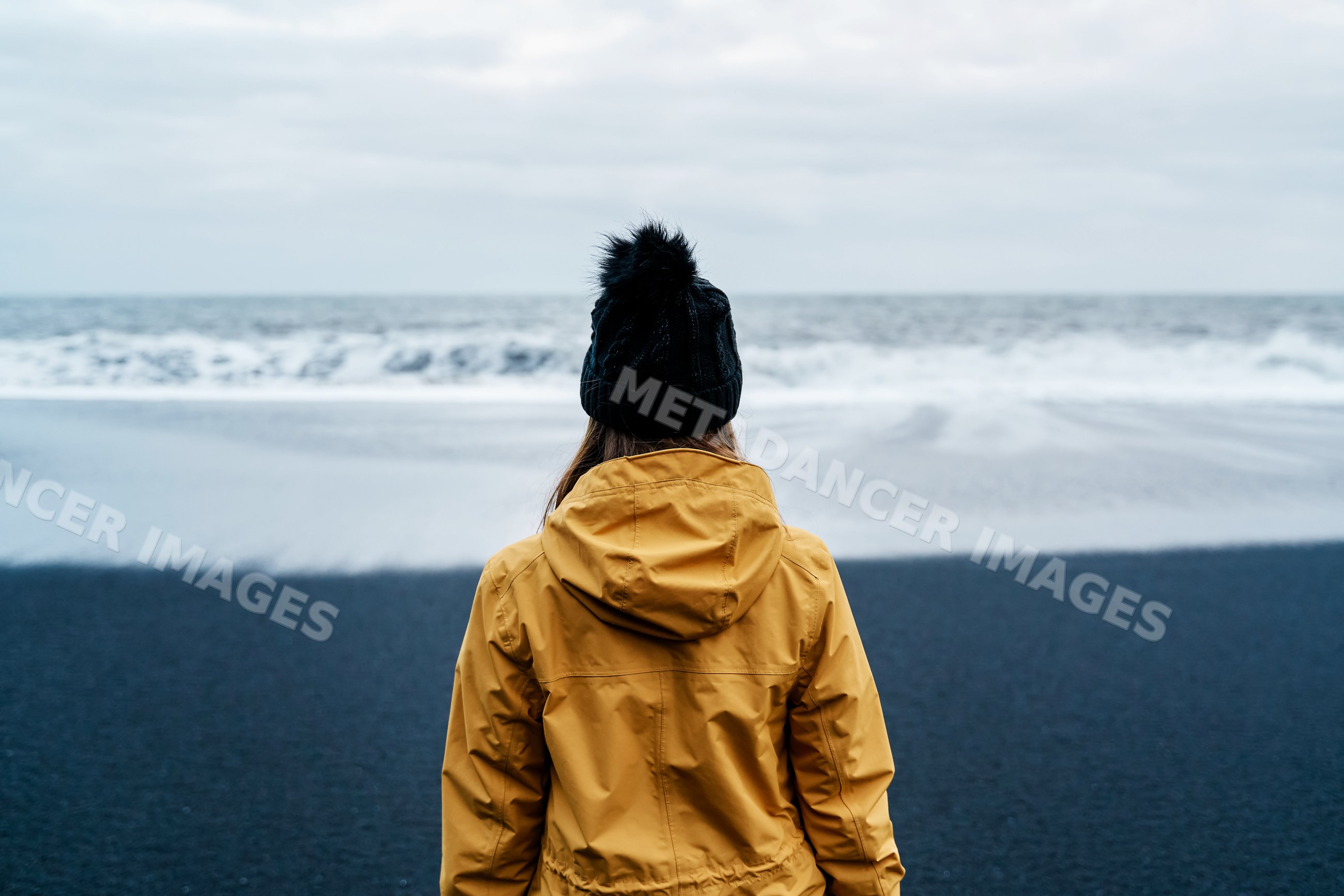 A white person in a yellow jacket looks out over the ocean
