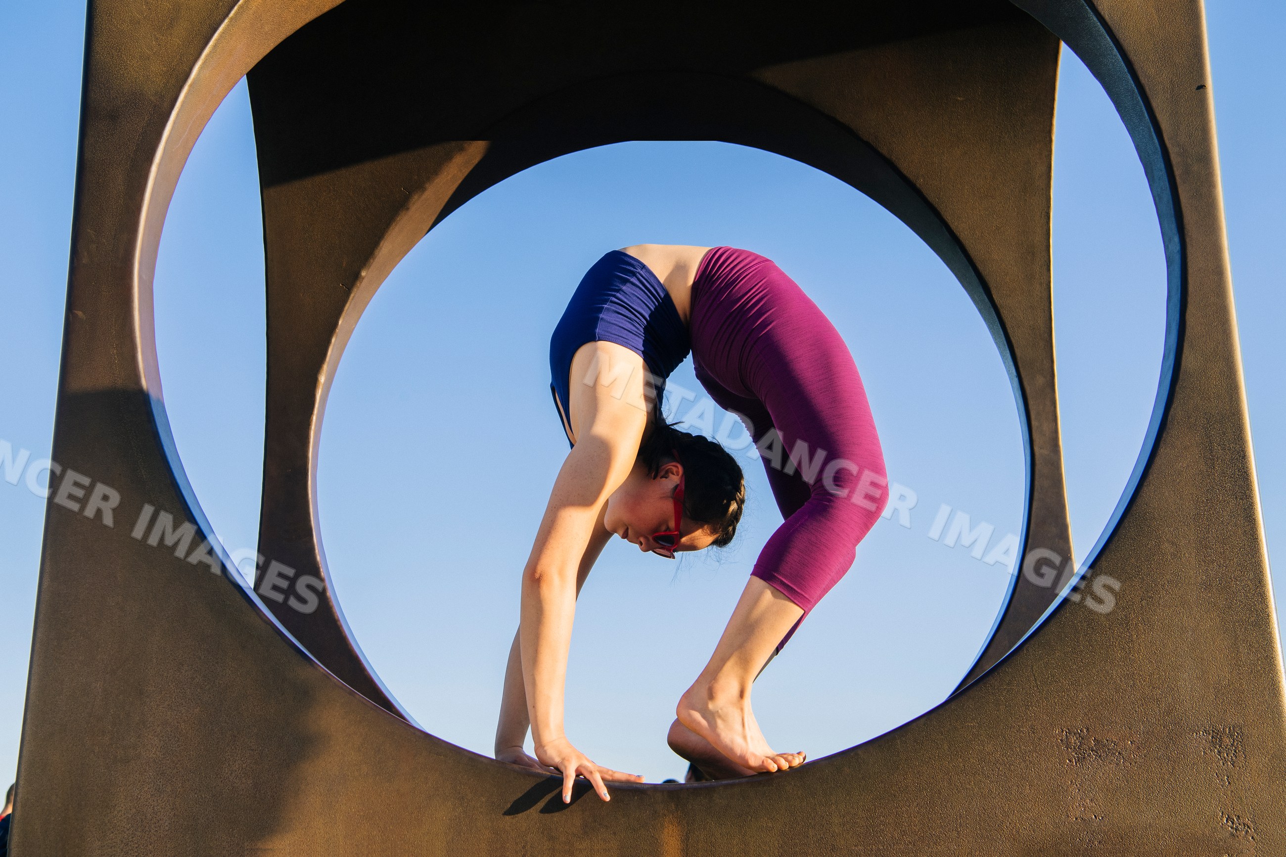 White woman performing backbend yoga pose framed by circular sculpture