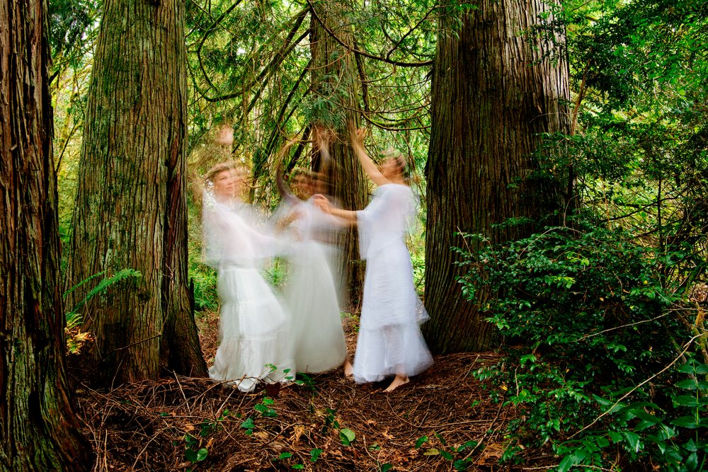 Women dancing in white dresses among forest trees with motion blur
