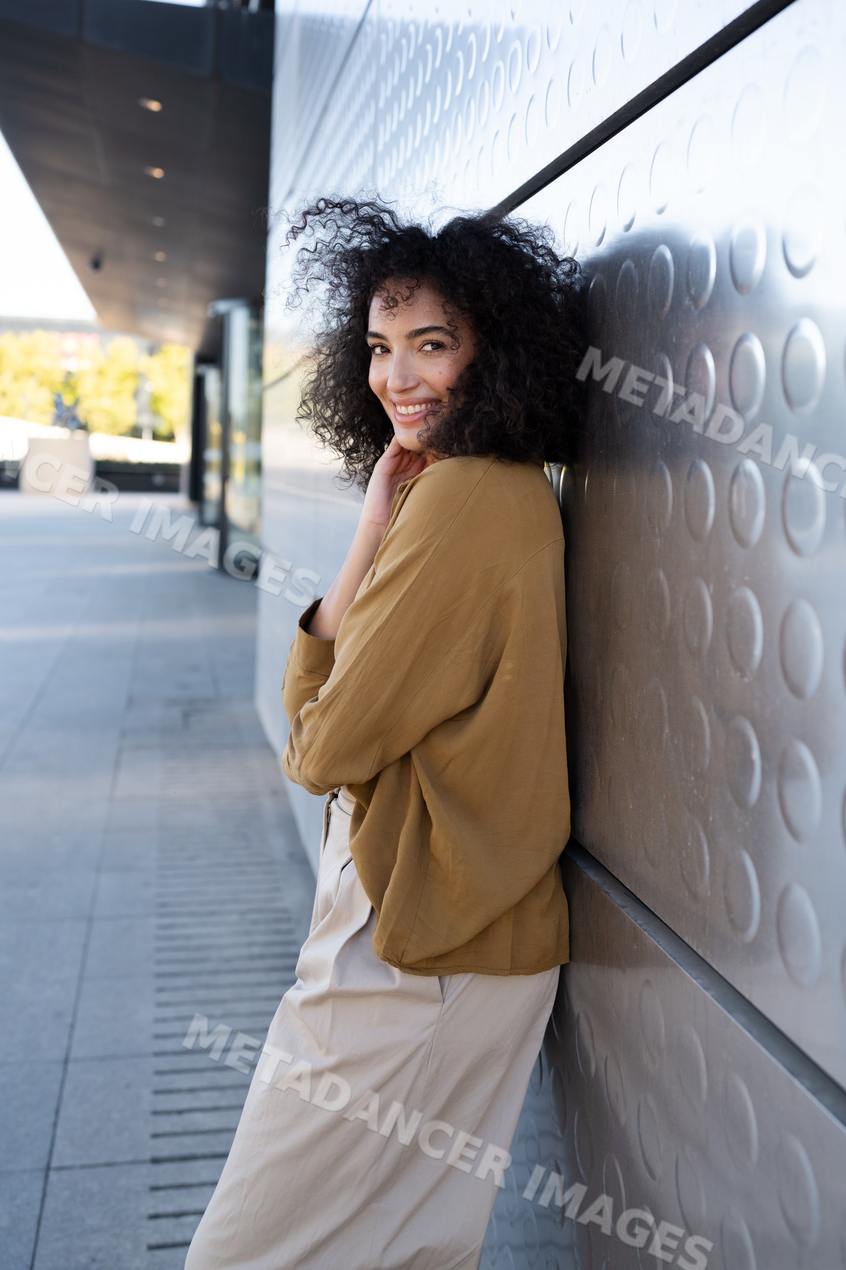 Woman with curly hair smiling outdoors by textured urban wall
