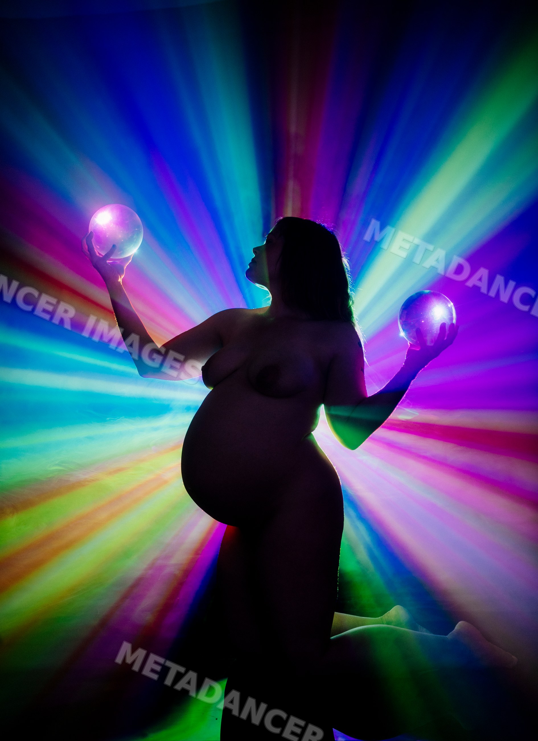 Pregnant silhouette kneeling with glowing spheres and rainbow light