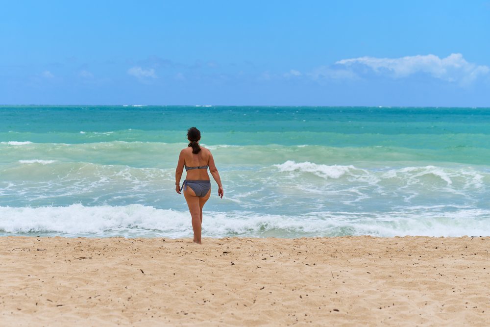 White woman walking toward ocean on sandy beach in a beach